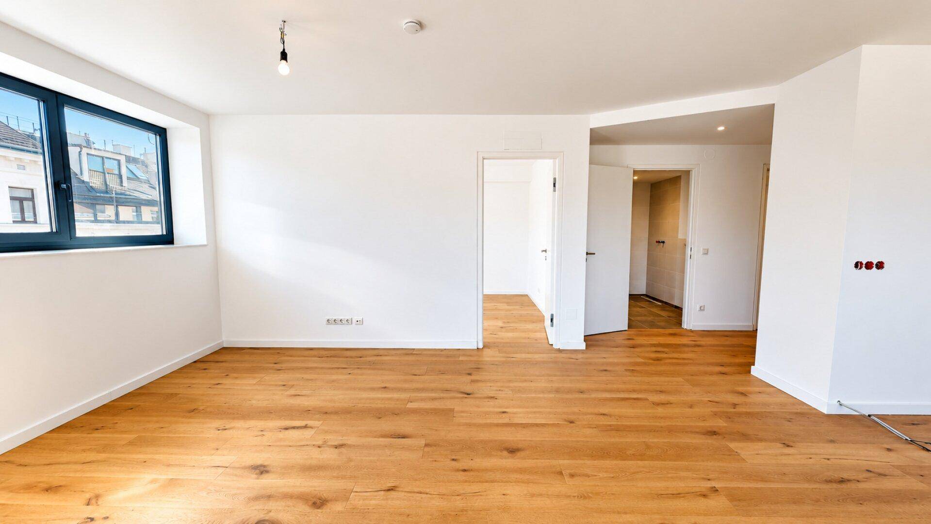Geräumiger, heller Wohnraum mit Holzboden und Blick in den Flur.