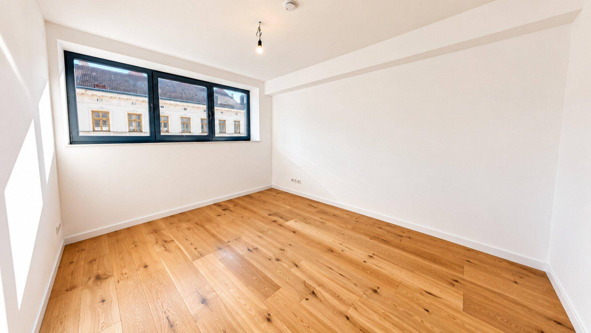 Helles Schlafzimmer mit Holzboden und Fenster, das einen Blick auf die Stadt bietet.