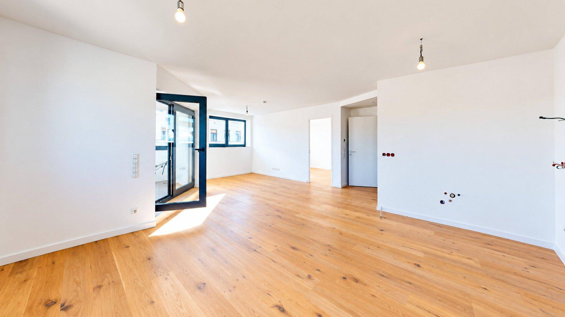 Geräumiges, leeres Wohnzimmer mit hellem Parkettboden und Zugang zu einem Balkon.