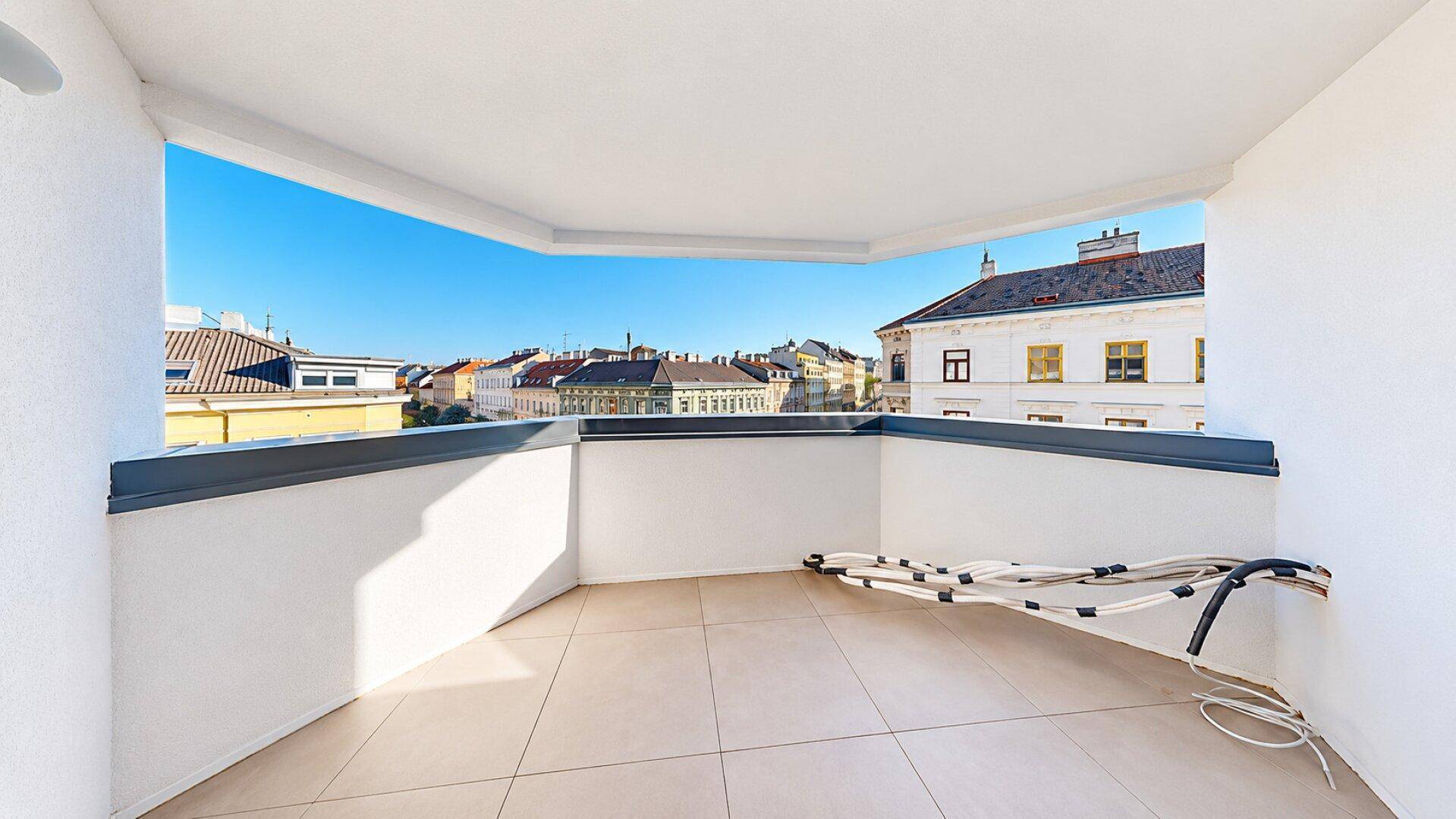 Leerer Balkon mit Fliesenboden und Stadtblick, bereit für Outdoor-Möbel.