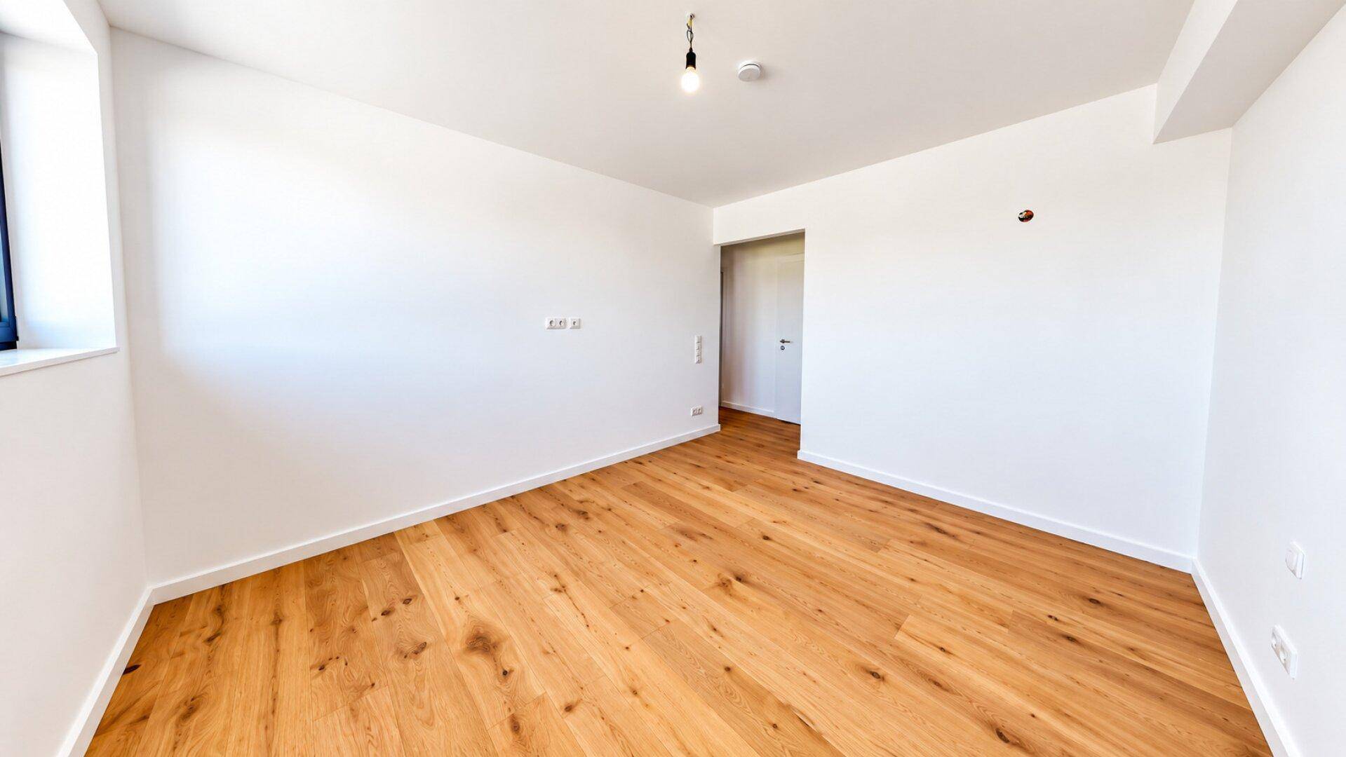 Helles Schlafzimmer mit Holzboden und weiß gestrichenen Wänden, mit Zugang zum Flur.