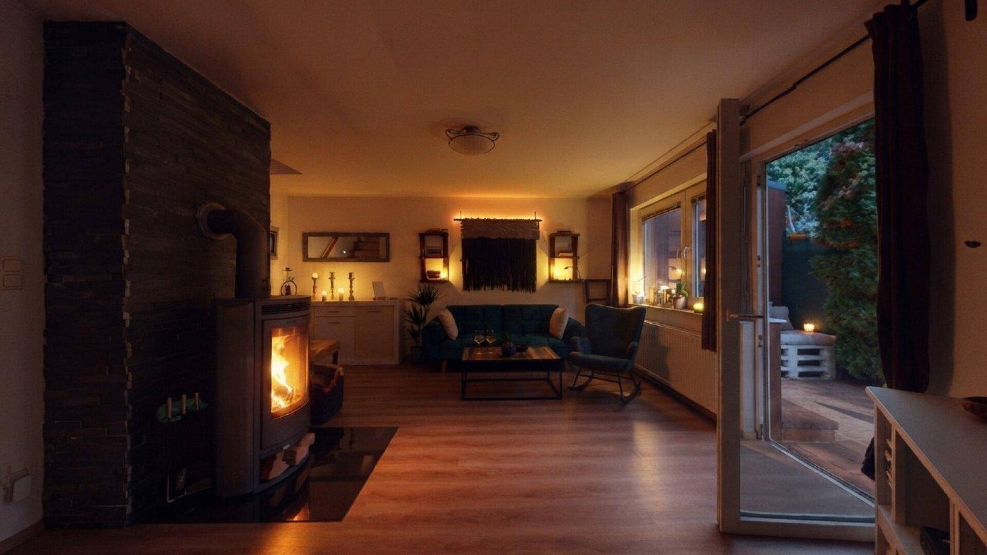 Stimmungsvoller Wohnbereich am Abend mit brennendem Kaminfeuer und direktem Terrassenzugang.