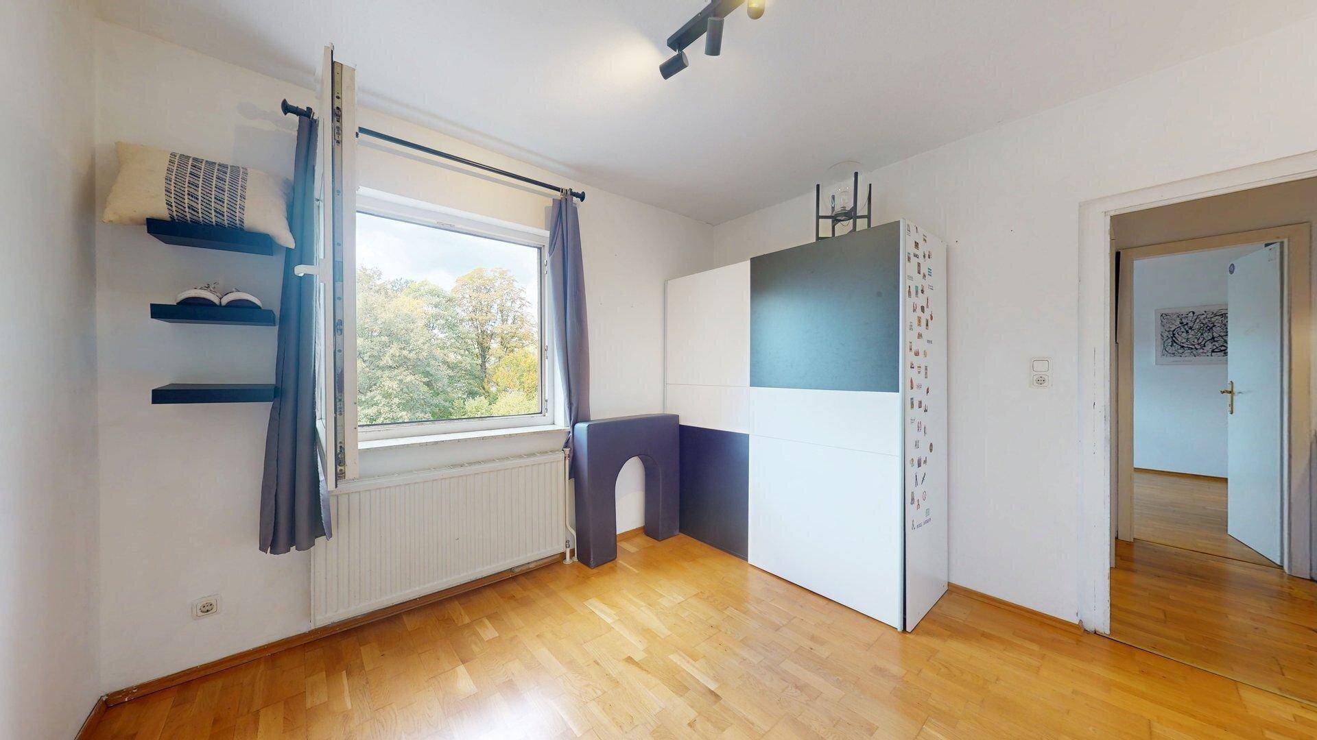 Helles Zimmer mit Holzboden, Fenster und schwebenden Regalen.
