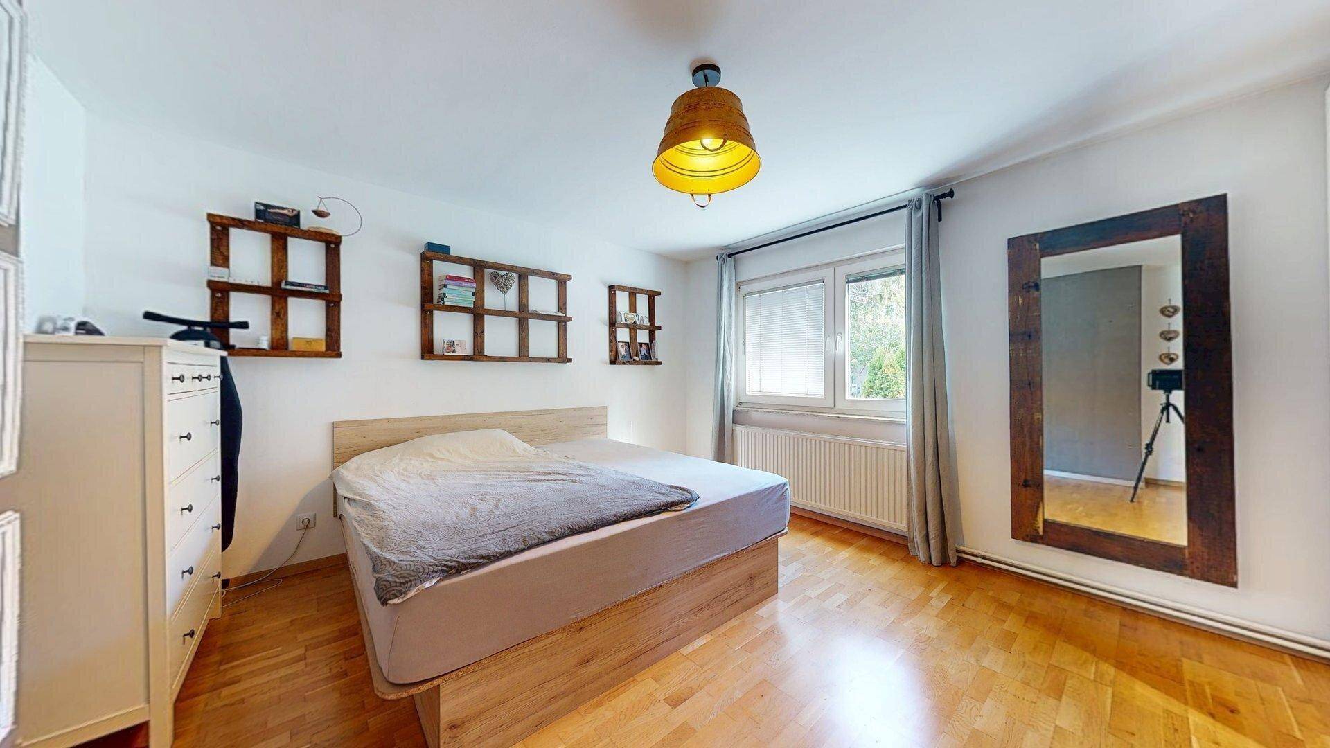 Gemütliches Schlafzimmer mit Holzbett, Parkettboden und großem Spiegel.