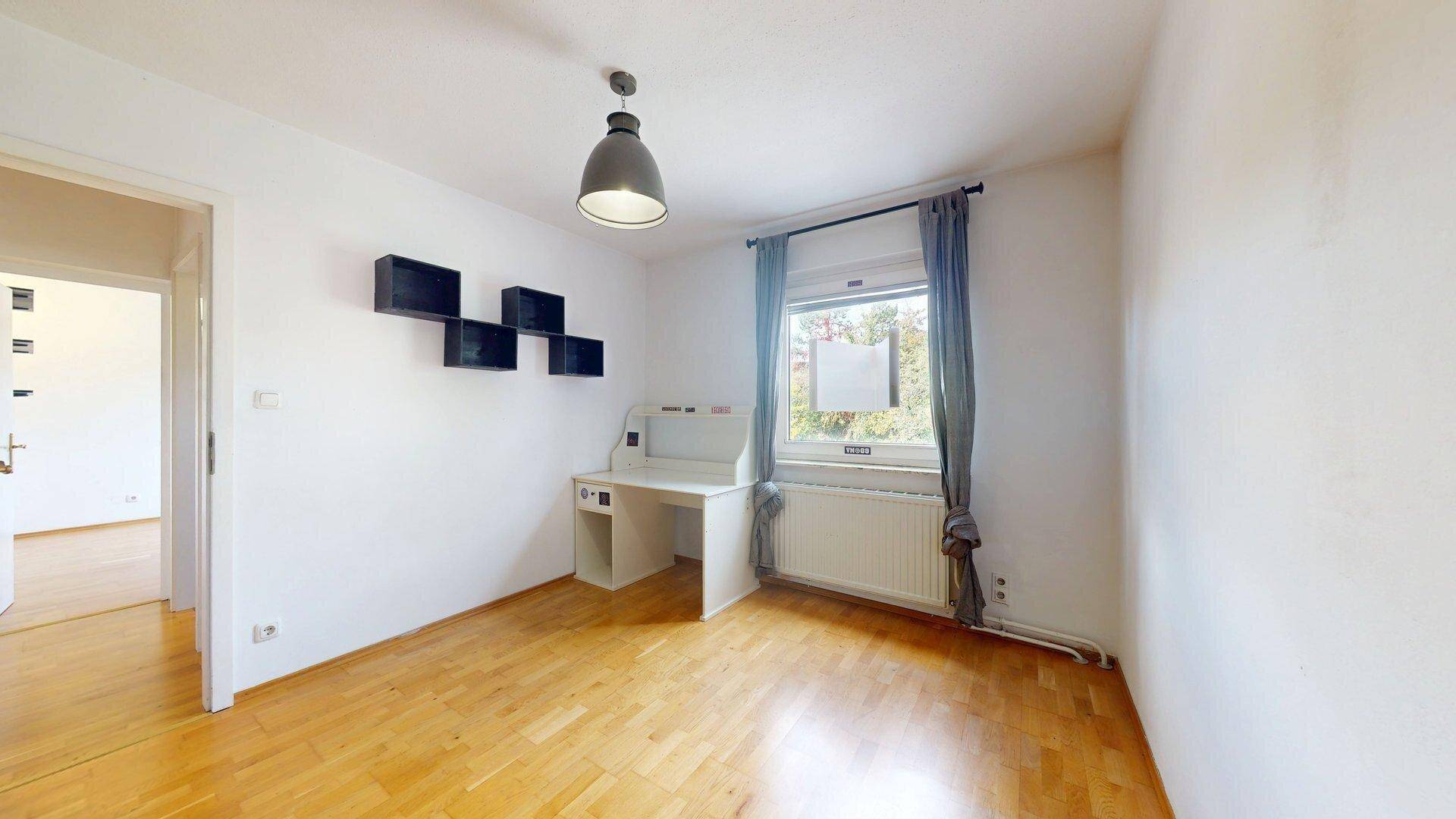 Freundliches Zimmer mit Schreibtisch, Holzboden und Fenster für viel Tageslicht.