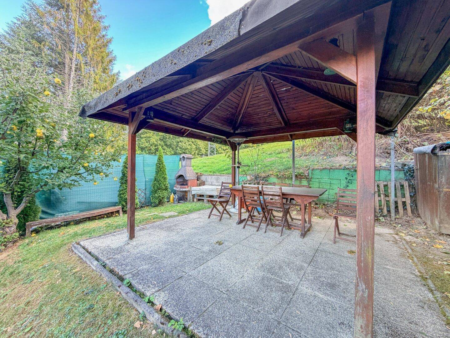 Überdachte Terrasse mit Grillplatz und Esstisch im Grünen, ideal für gesellige Abende.