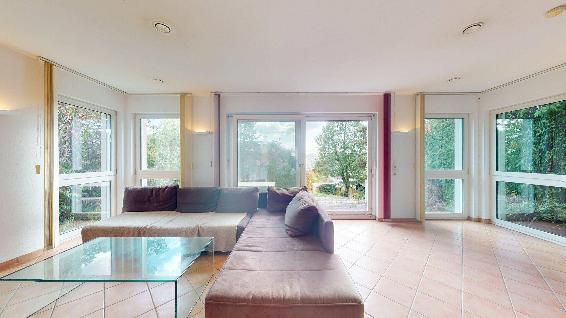 Geräumiges Wohnzimmer mit bequemer Couch, großen Fensterfronten und direktem Zugang zum Außenbereich.