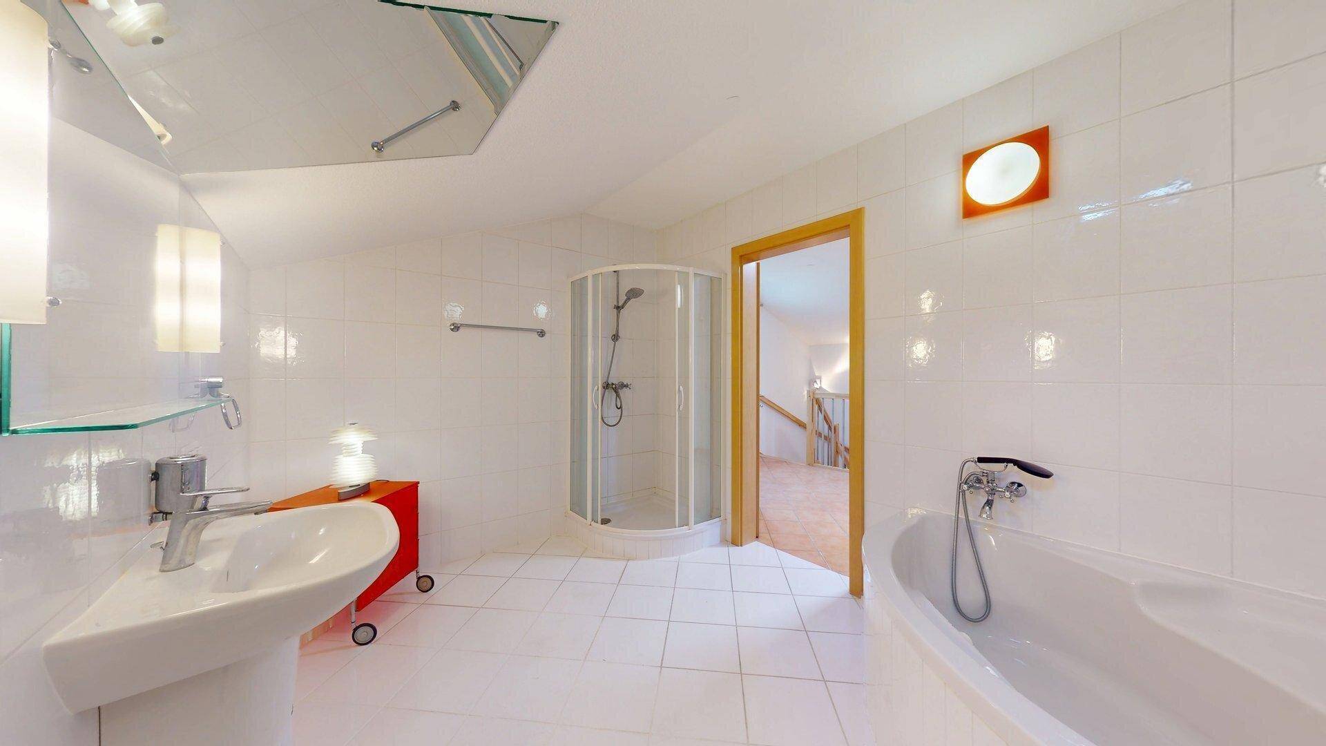 Helles Badezimmer mit weißen Fliesen, Dusche, Badewanne und einem Oberlicht für natürliches Licht.