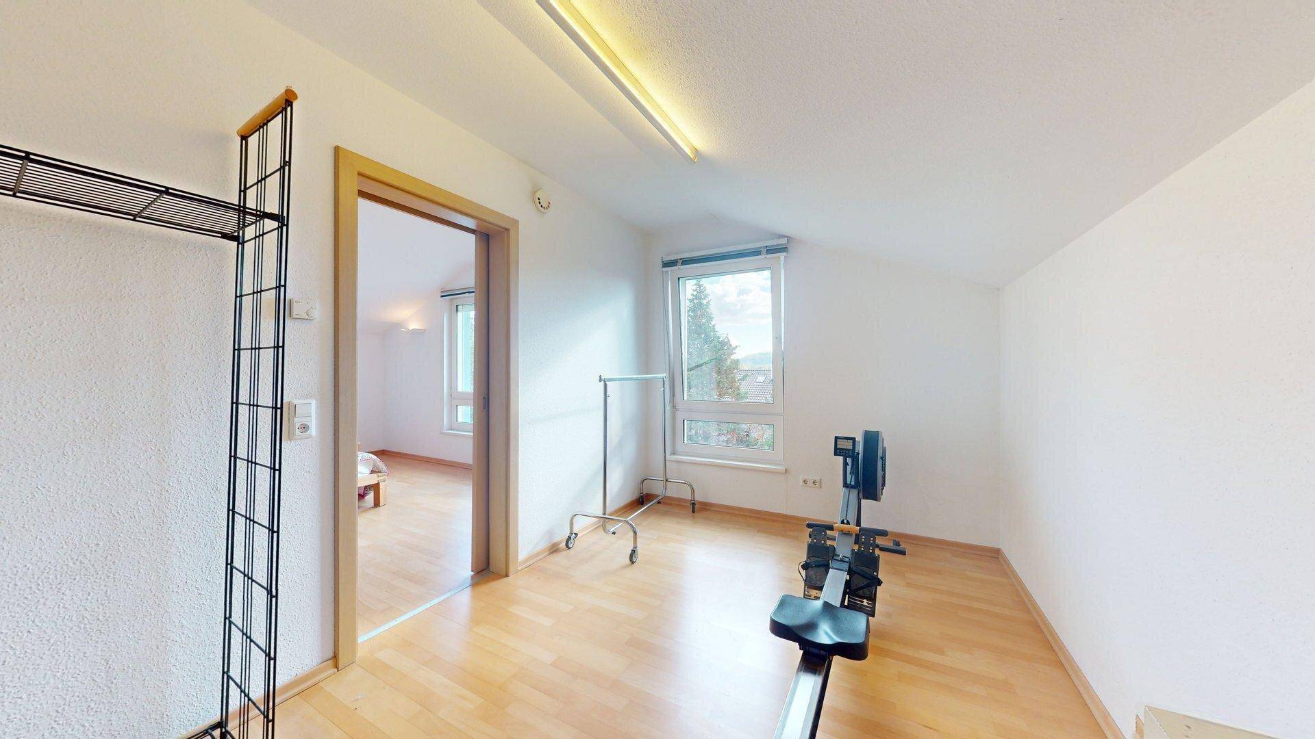 Flexibler Raum mit Holzboden, Fenster und Dachschräge, ideal als Büro oder Fitnessbereich nutzbar.