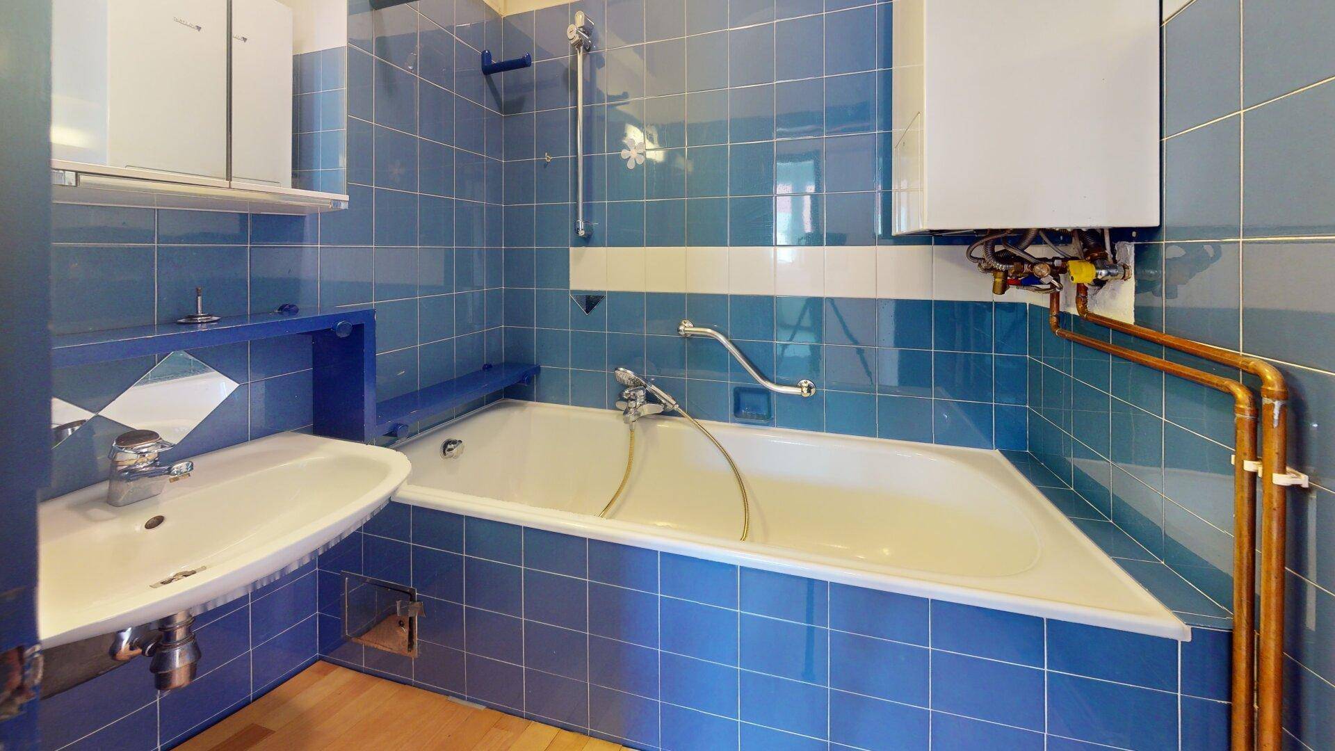Badezimmer mit blauen Fliesen, einer Badewanne und einem Waschbecken, in einem älteren, aber funktionalen Zustand.