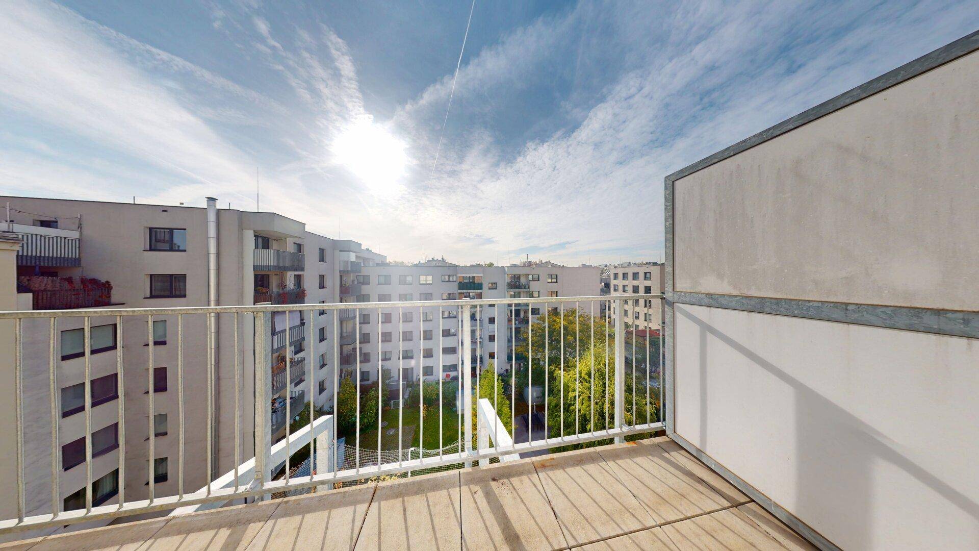 Geräumiger Balkon mit Holzboden und weitem Blick über die umliegenden Wohngebäude und den Himmel.