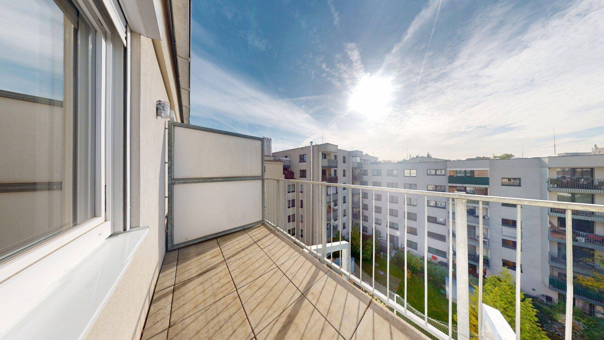Sonniger Balkon mit Holzboden und weitem Blick über die Stadt und die umliegenden Wohngebäude.