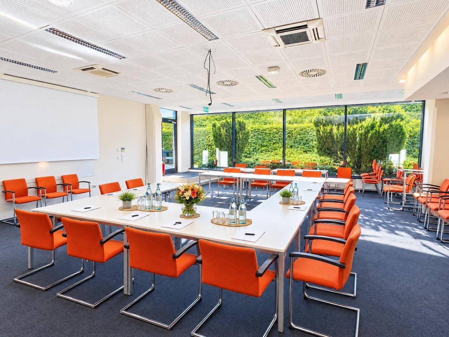 Großer Konferenzraum mit U-förmigem Tisch, vielen Stühlen und Blick ins Grüne durch Panoramafenster.