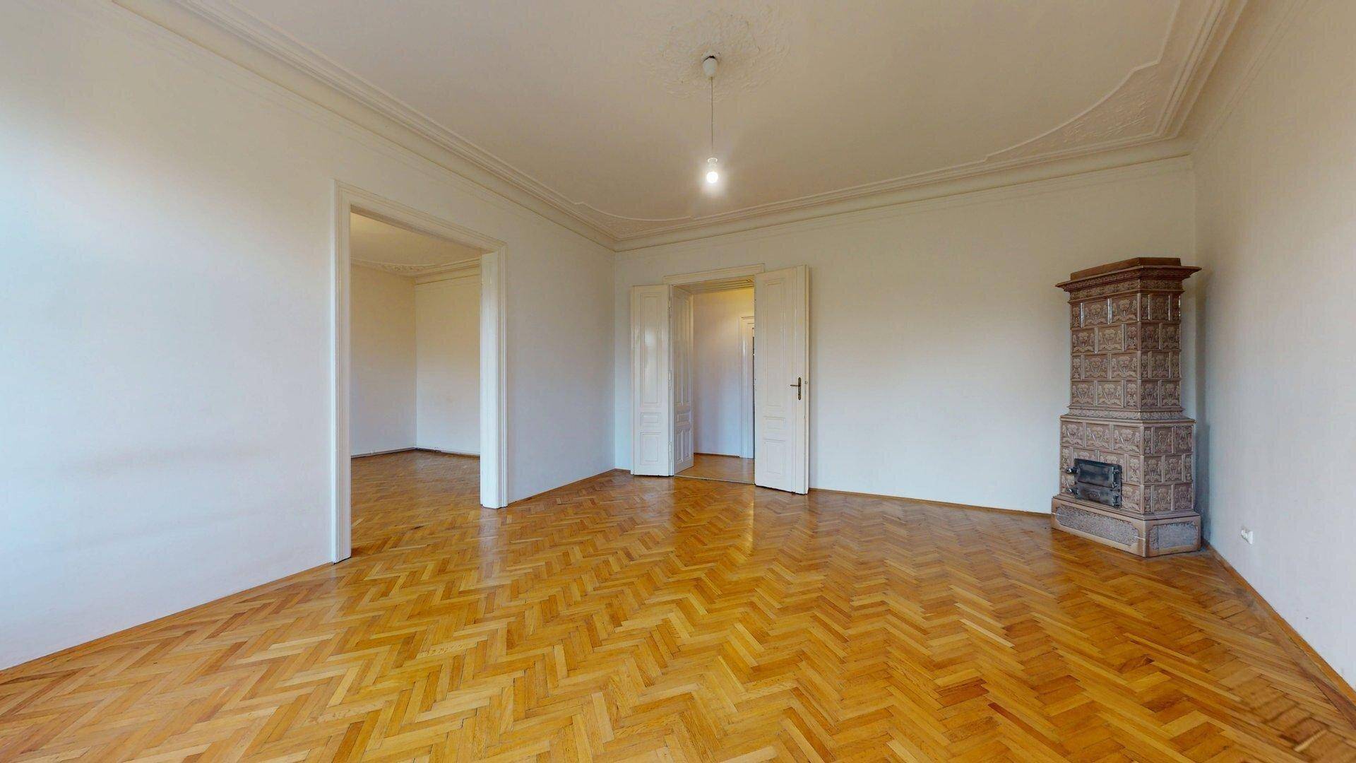 Großes Wohnzimmer mit traditionellem Kachelofen, Fischgrätparkett und hohen Decken, ideal für gemütliche Abende.