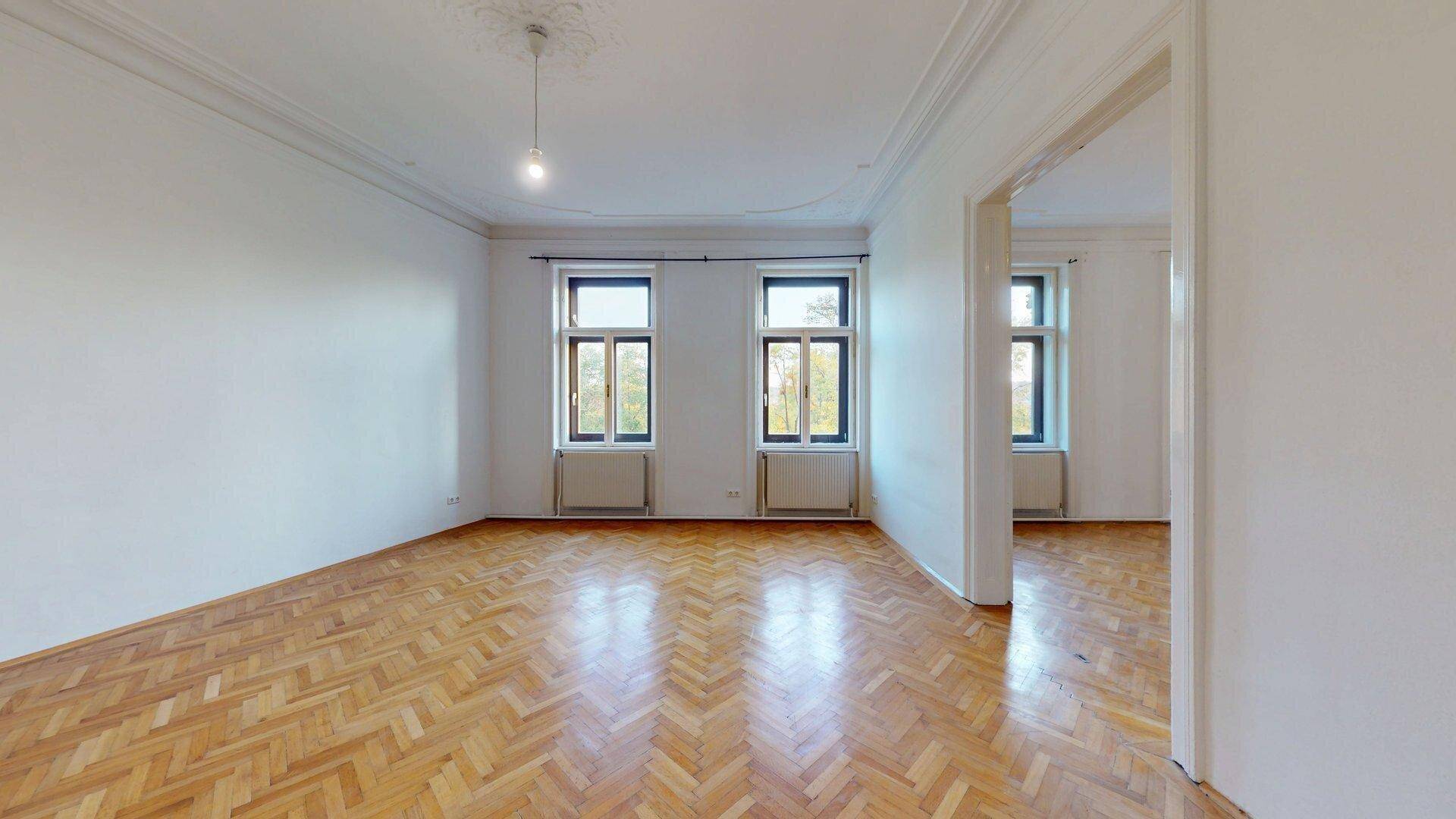 Lichtdurchfluteter Raum mit Fischgrätparkett und hohen Decken, der vielseitig als Wohn- oder Esszimmer genutzt werden kann.