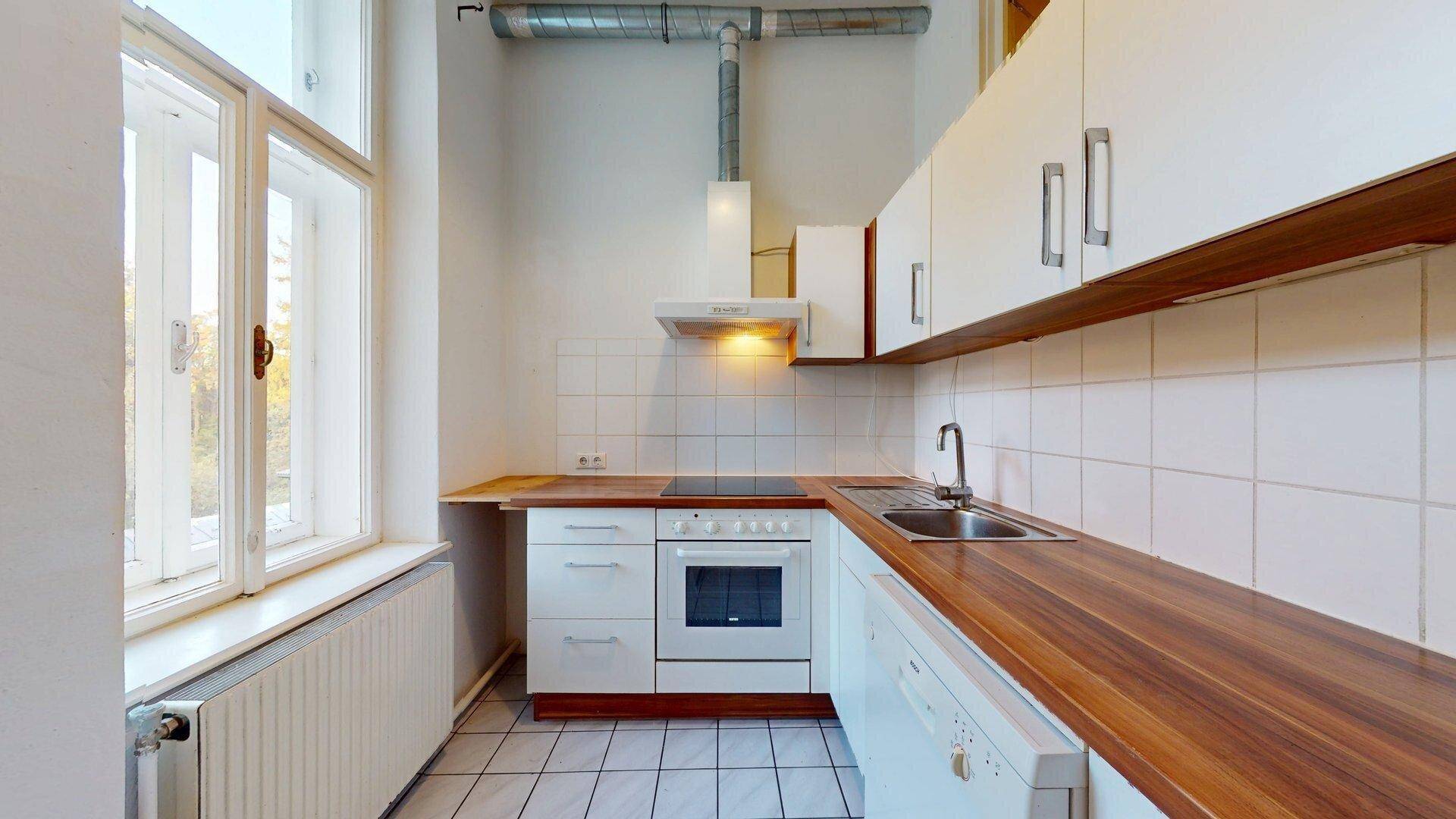 Funktionale Küche mit Holz-Arbeitsplatten, weißen Schränken, Fenster und integrierten Geräten.