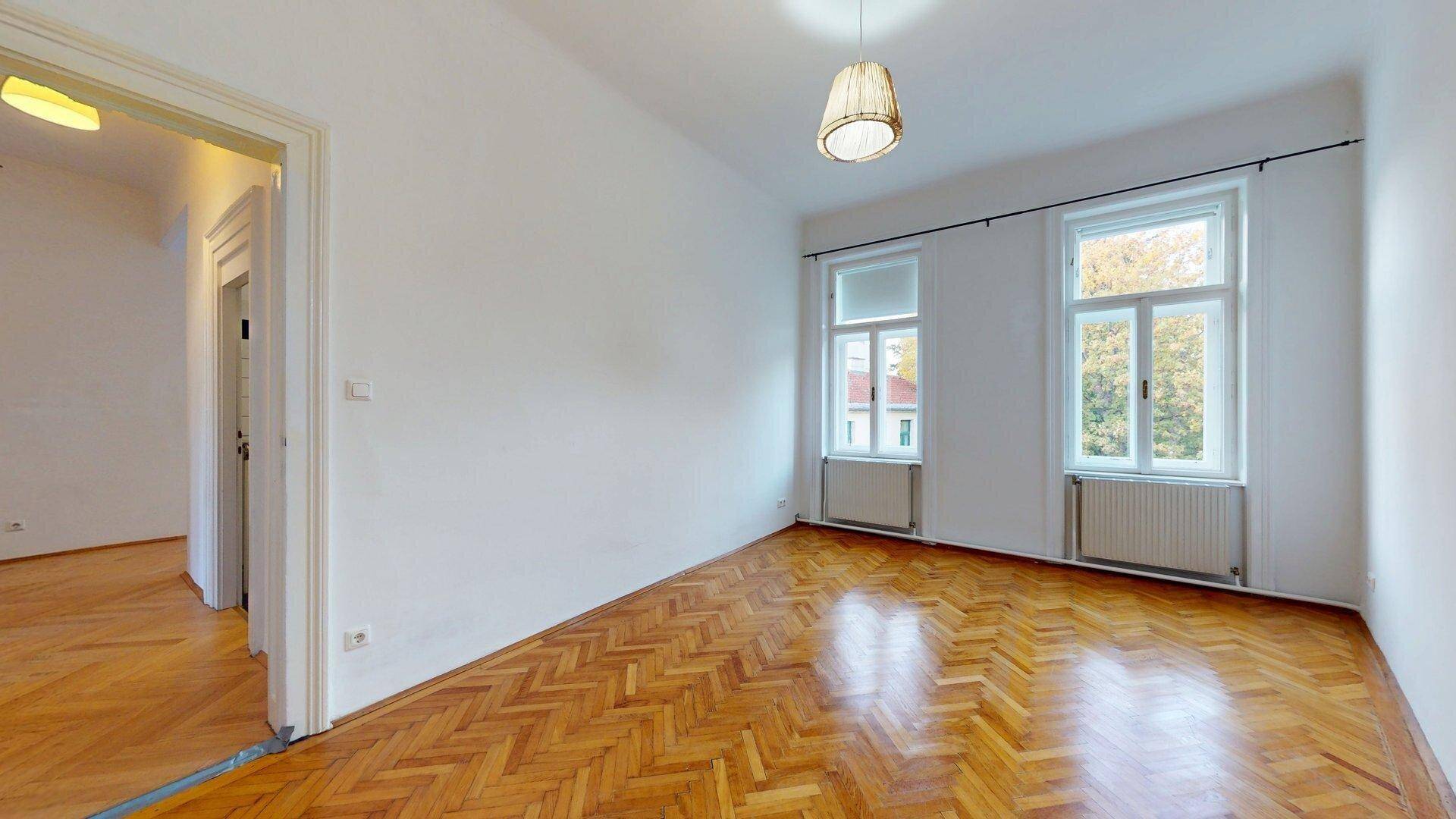 Helles Zimmer mit Fischgrätparkett und zwei Fenstern, ideal als Schlafzimmer oder Arbeitszimmer nutzbar.
