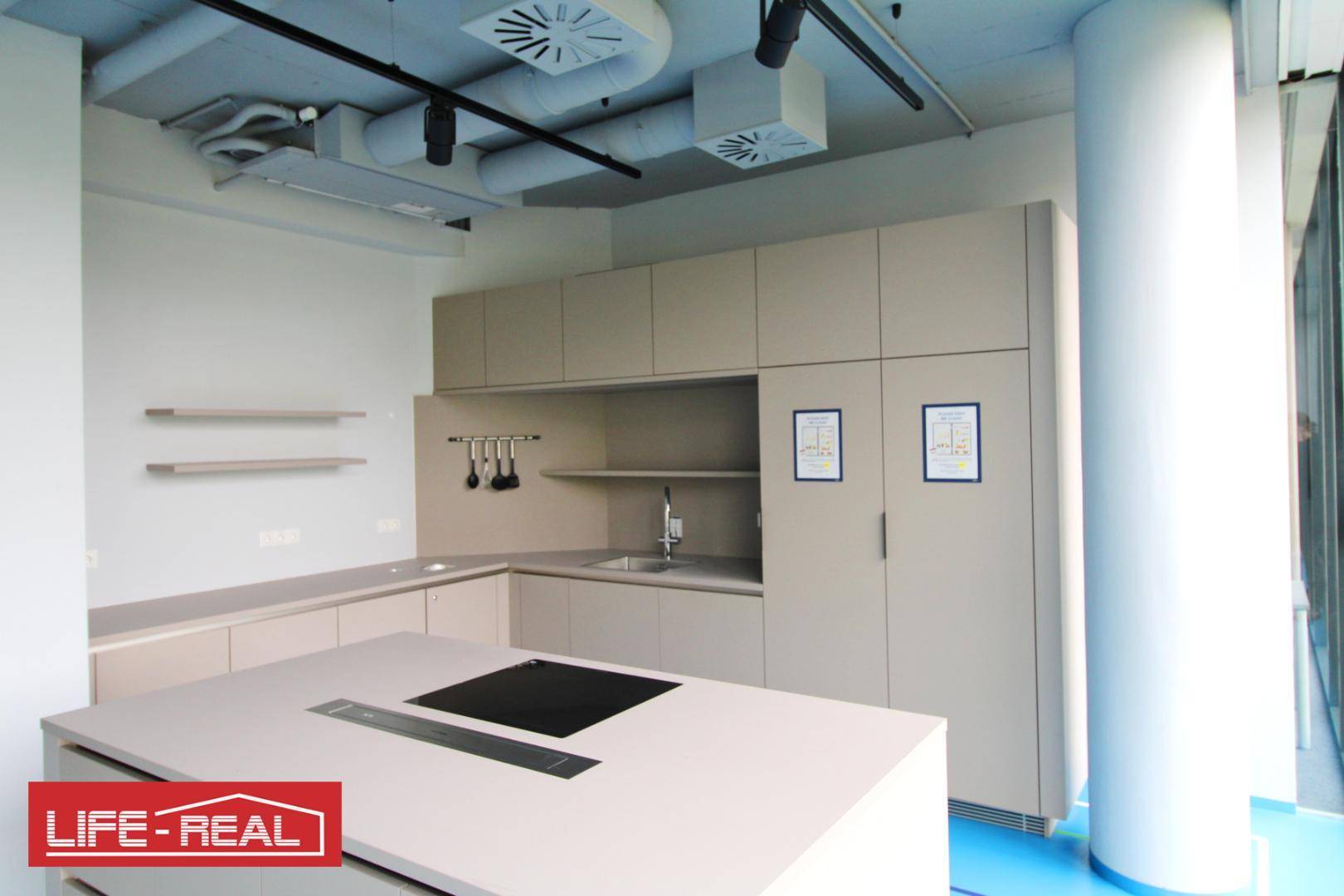 Moderne Küche mit Kücheninsel, Induktionskochfeld und freiliegenden Lüftungsrohren in einem Neubau mit hohen Decken.