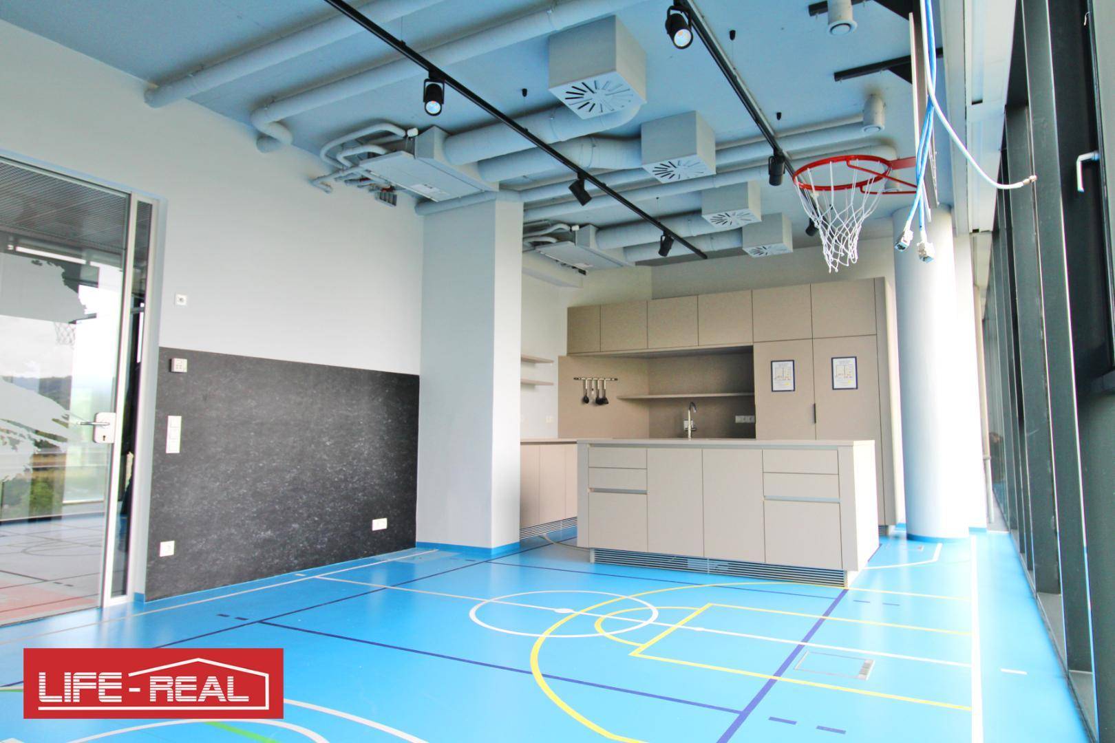 Freizeitraum mit Basketballkorb, Küchenzeile und freiliegenden Deckeninstallationen.