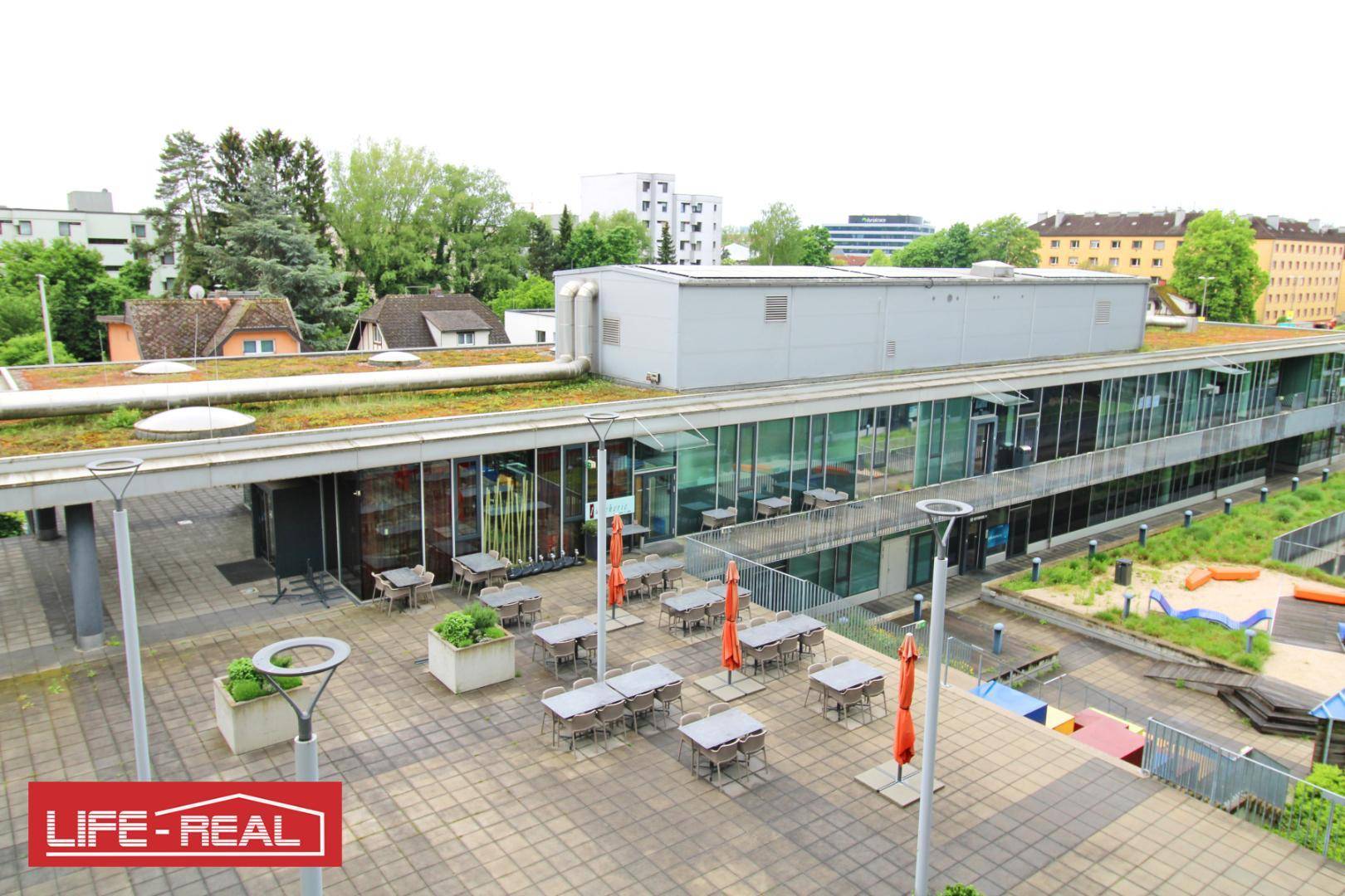 Außenterrasse eines Bürogebäudes mit Tischen, Sonnenschirmen und Blick auf die Umgebung.
