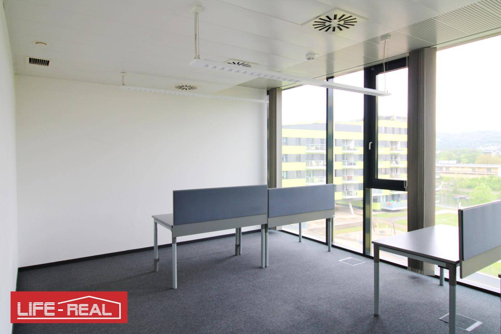 Büro mit Schreibtischen, großen Fenstern und Blick auf die umliegenden Gebäude.