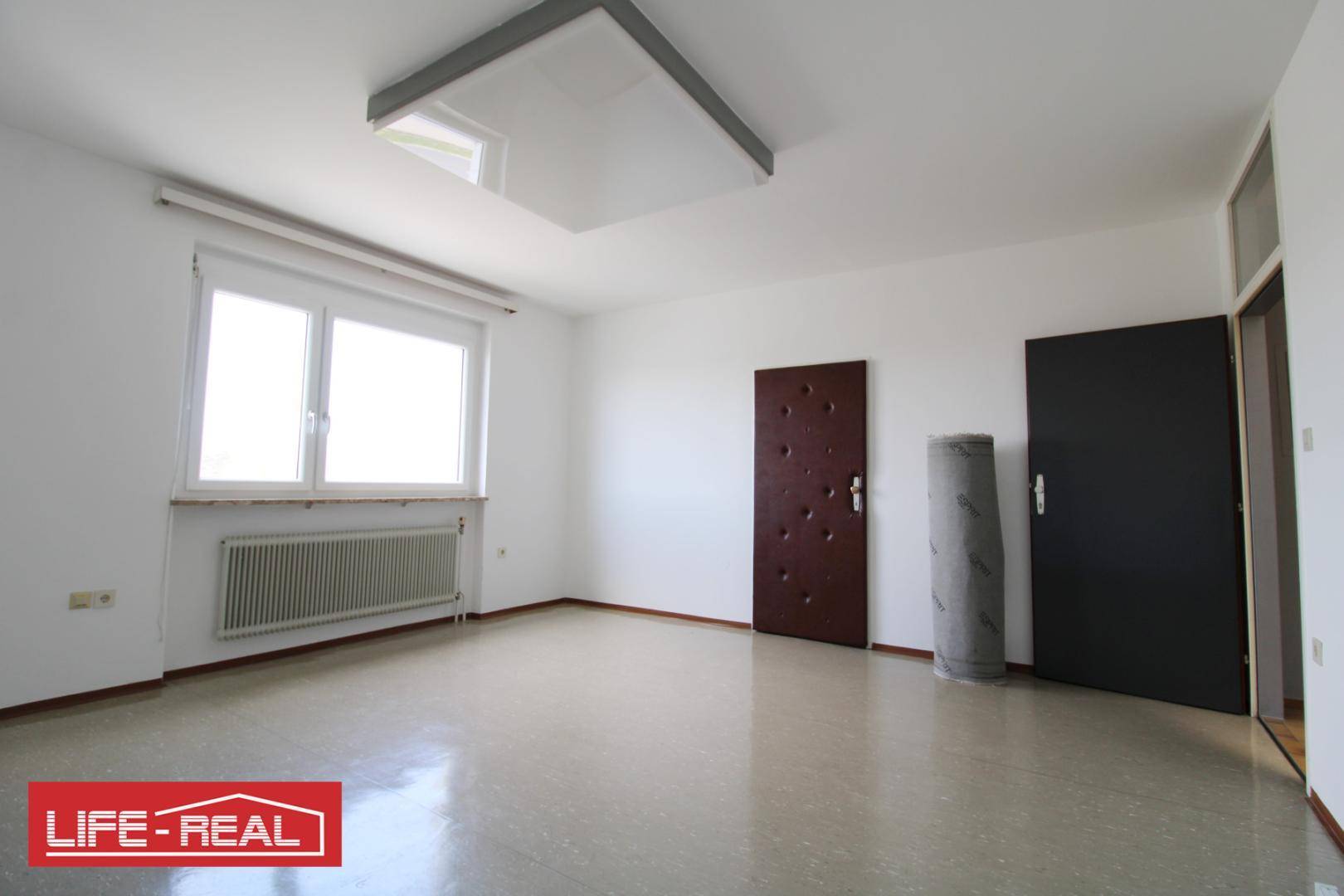 Leerer Raum mit Fenster, Heizkörper und zwei Türen, bereit für eine neue Nutzung oder Einrichtung.