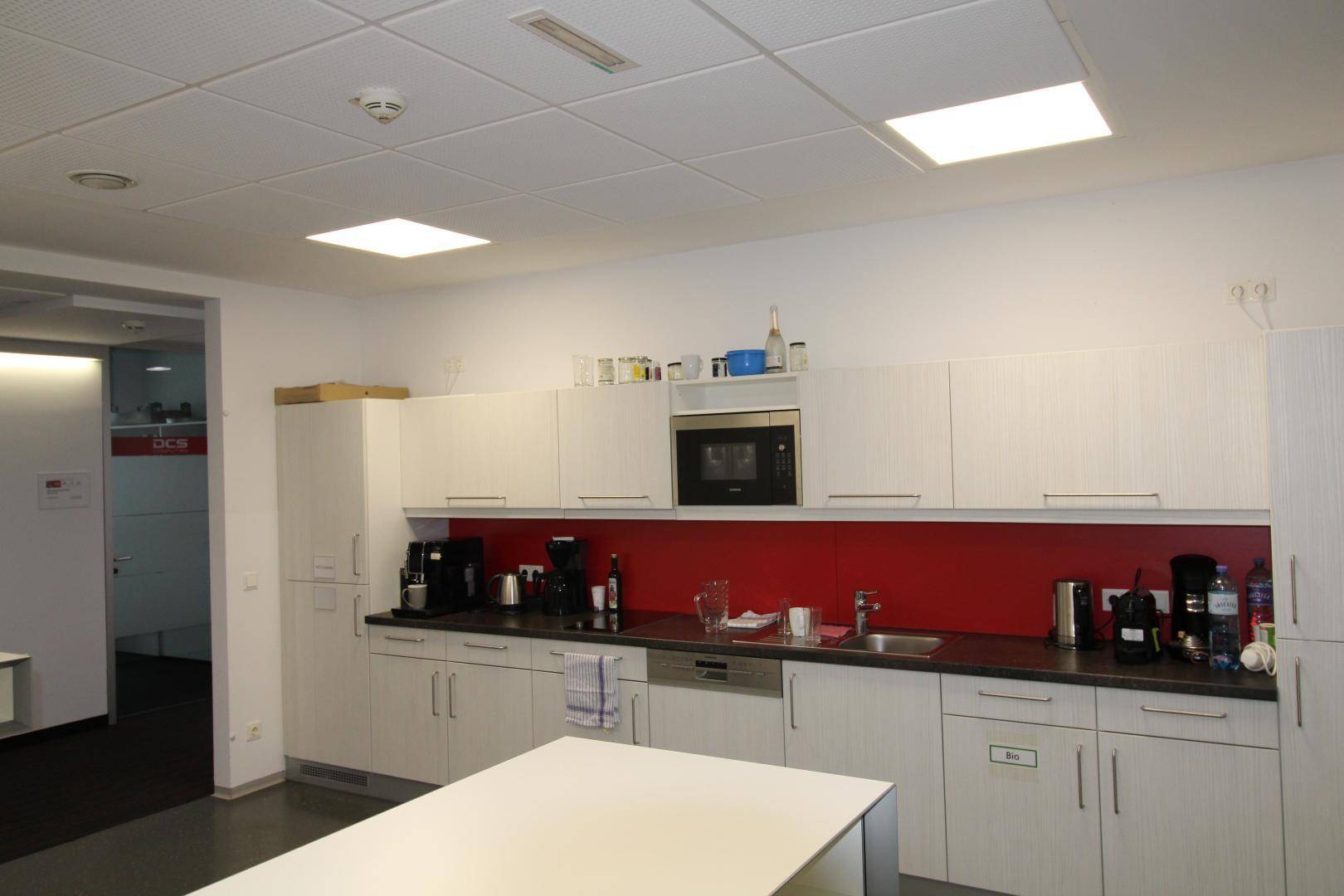 Moderne Einbauküche mit weißen Schränken, roter Rückwand und integrierten Geräten, ideal für Mitarbeiter.