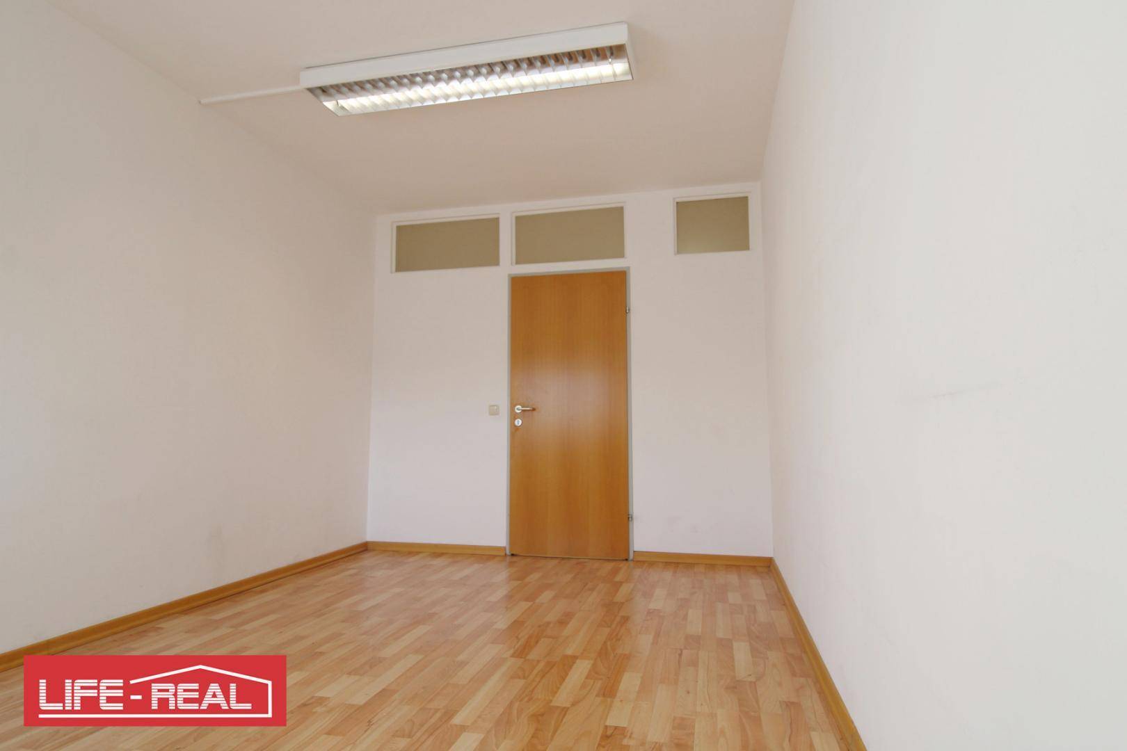 Unmöbliertes Büro mit Laminatboden und einer Holztür mit Oberlichtern, bietet viel Potenzial.