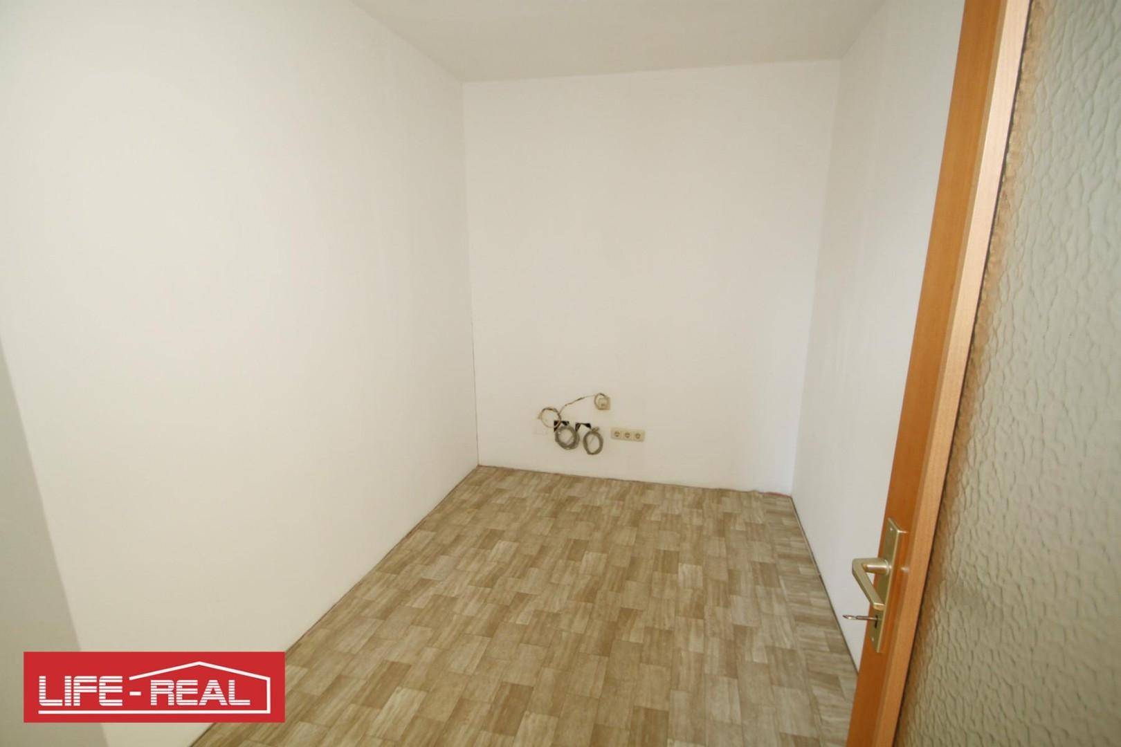 Kleiner, leerer Raum mit Laminatboden, weißen Wänden und einer Tür, vorbereitet für Installationen.