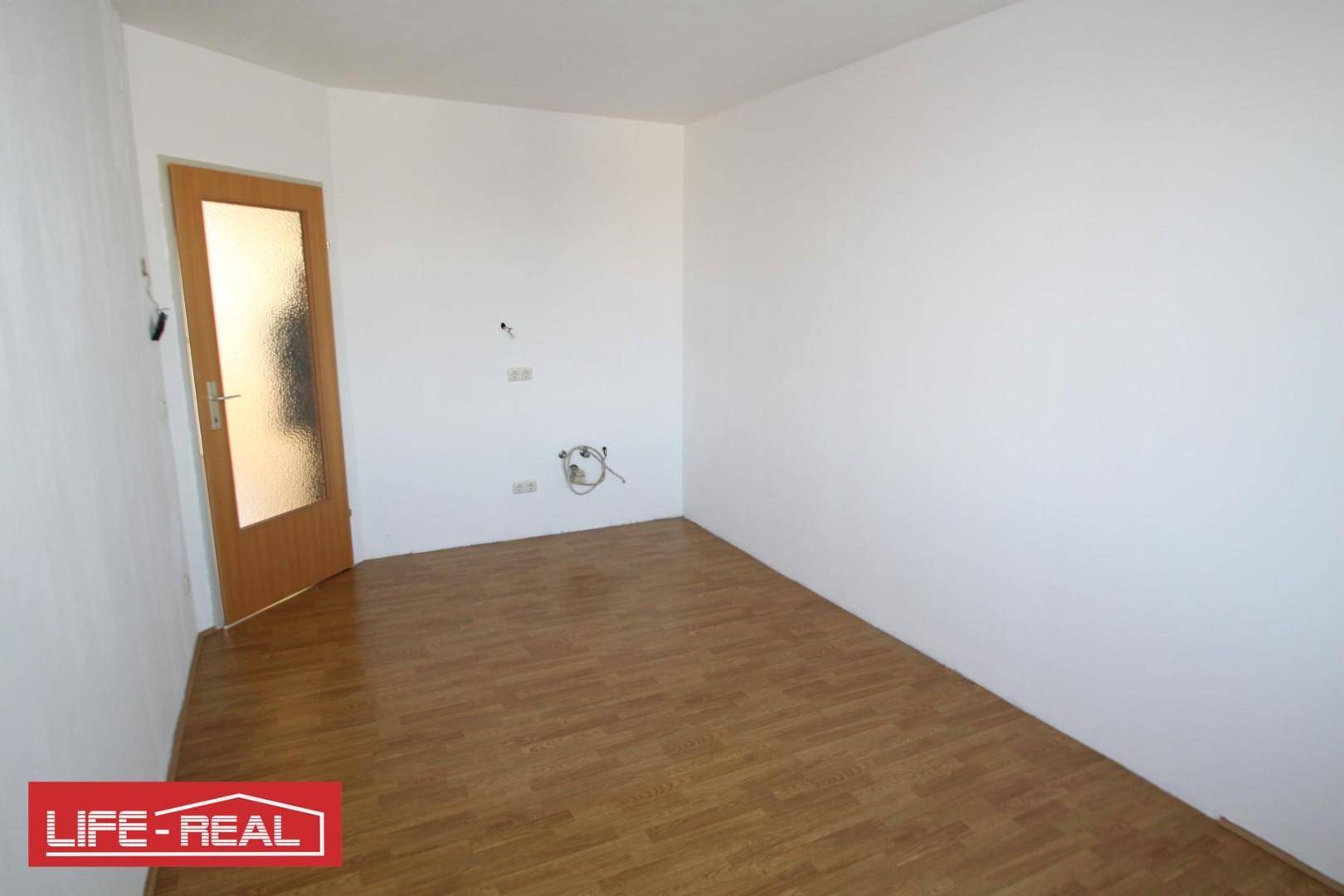 Leerer Raum mit Laminatboden, weißen Wänden und einer Holztür mit Milchglas, vorbereitet für Anschlüsse.