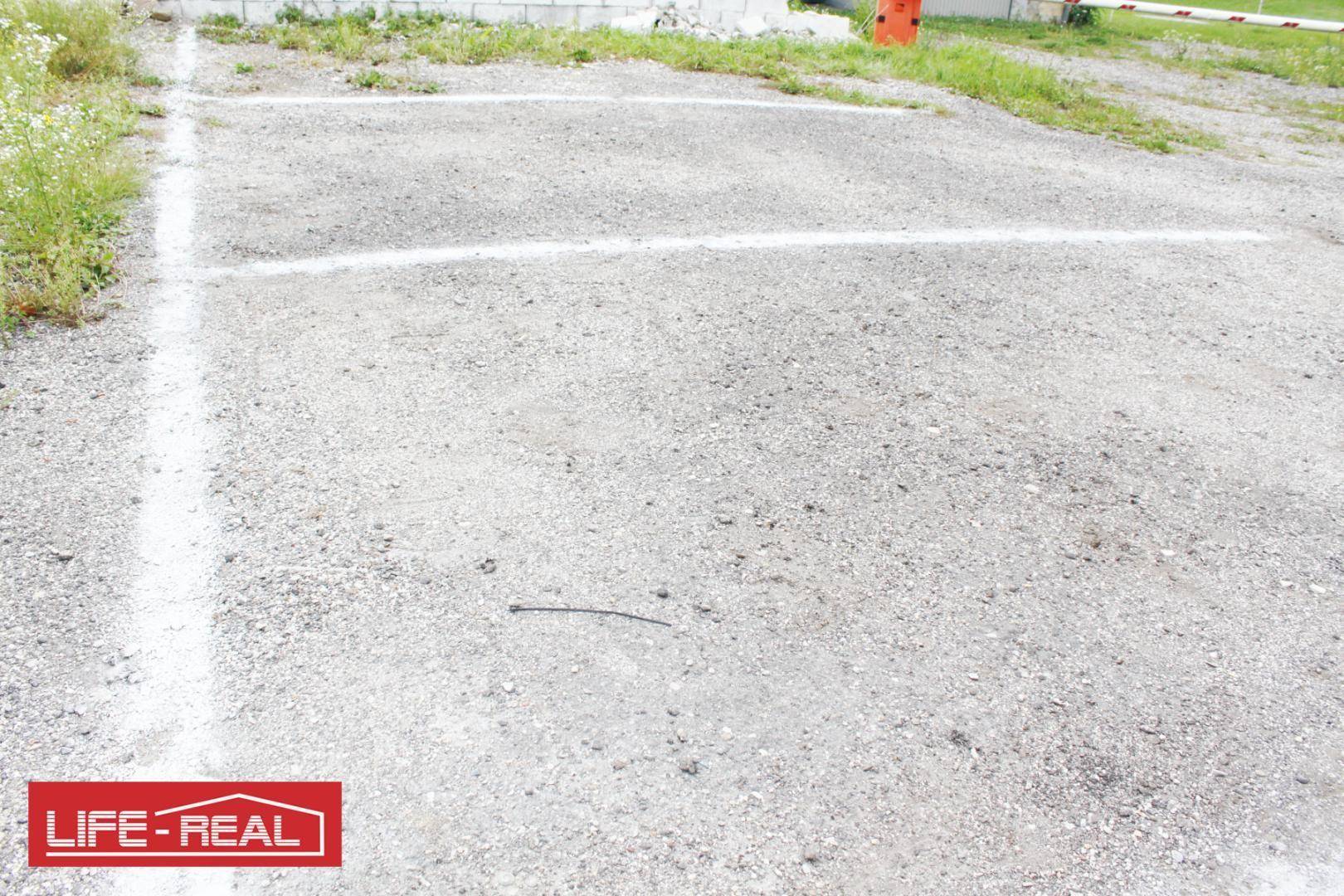 Unbefestigter Parkplatz mit Schotteroberfläche und deutlichen weißen Parkplatzmarkierungen.