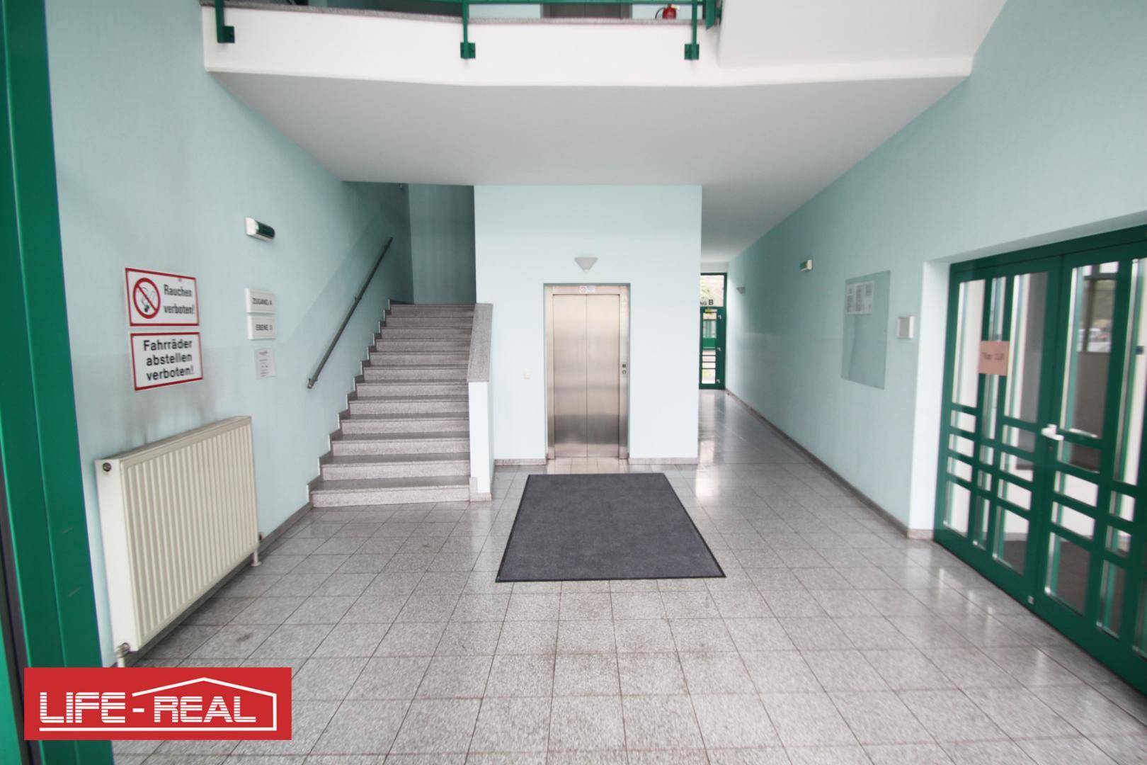 Heller Eingangsbereich mit Aufzug, Treppenhaus und Fliesenboden, der zu den Wohneinheiten führt.