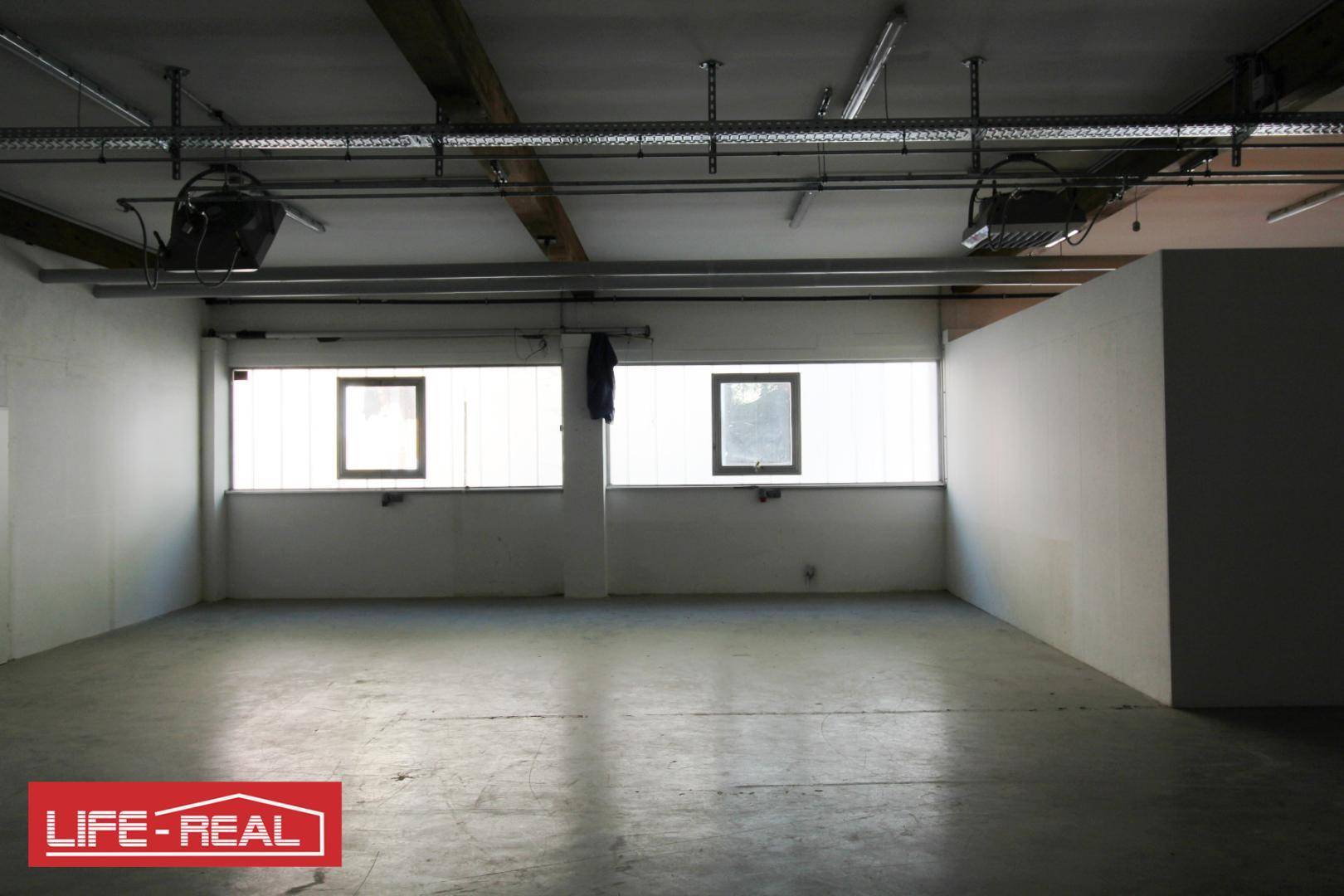 Heller Lagerraum mit Betonboden und großen Fenstern, bietet viel Tageslicht und Platz.