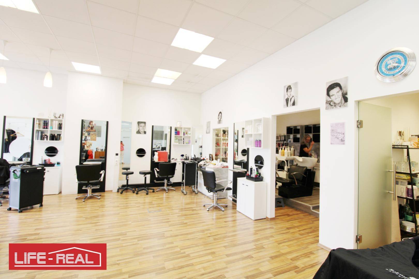 Geräumiger Friseursalon mit mehreren Arbeitsplätzen, großen Spiegeln und Holzfußboden.