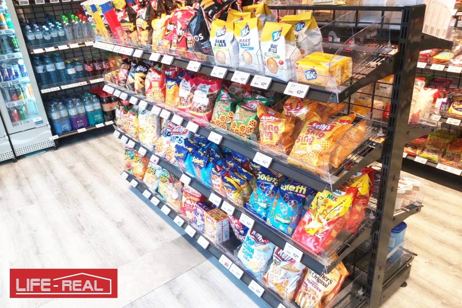 Innenansicht eines modernen Ladenlokals mit Regalen voller verpackter Snacks und Süßigkeiten.