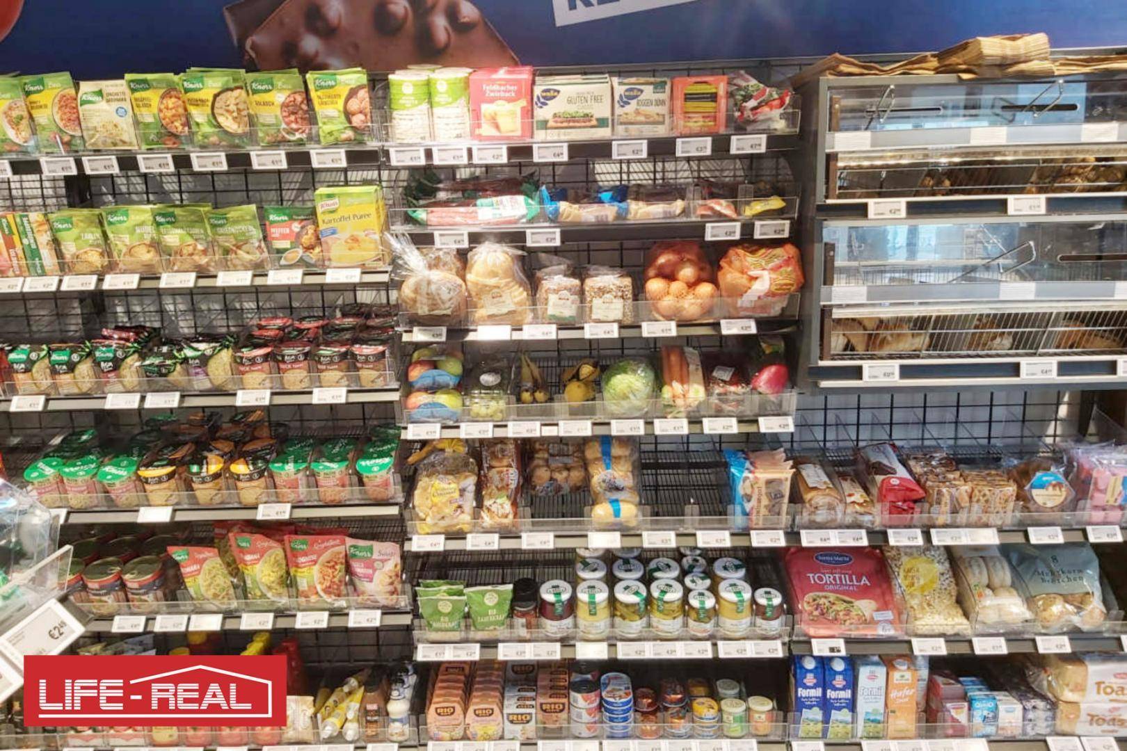 Vielfältiges Angebot an verpackten Lebensmitteln, frischem Brot und Gemüse in den Regalen des Ladens.