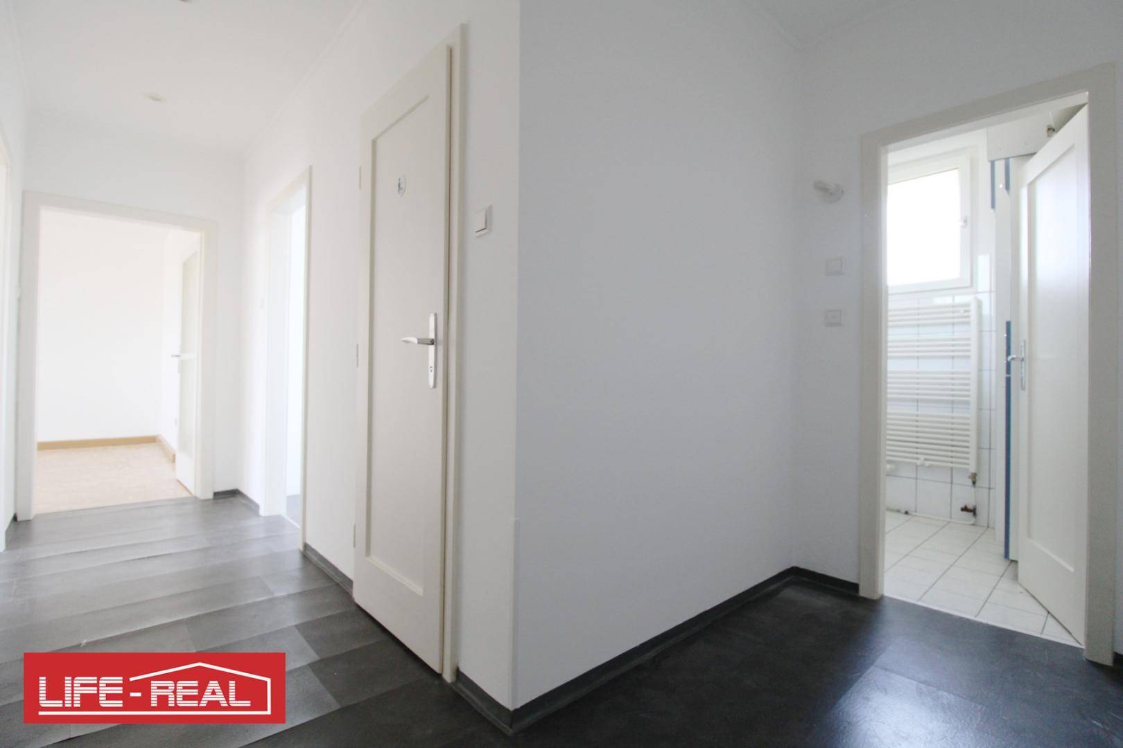 Heller Flur mit dunklem Bodenbelag, der zu verschiedenen Zimmern führt.