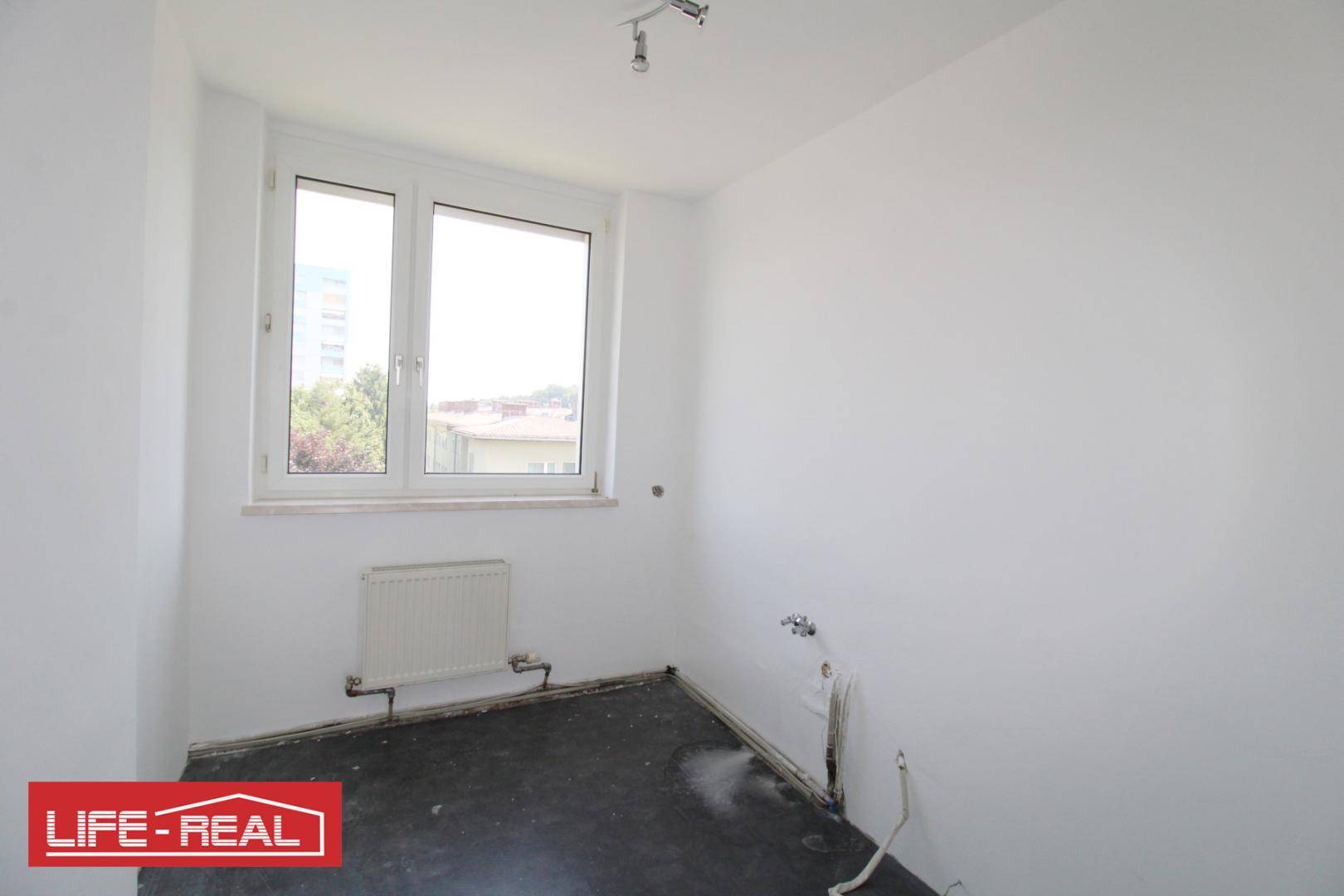 Leerer Küchenraum mit Anschlüssen für Geräte und Fenster, bereit für eine neue Einbauküche.