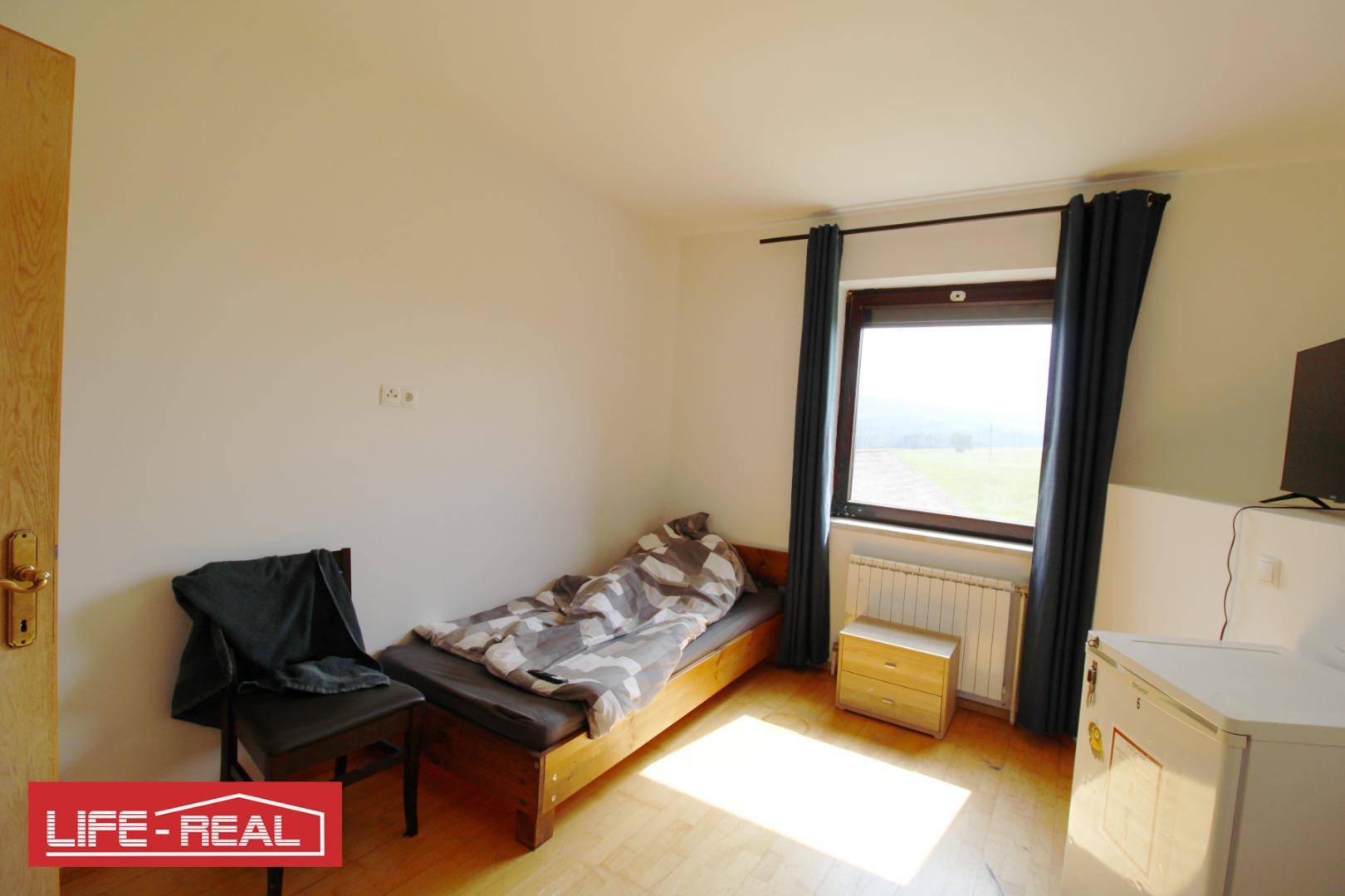 Helles Schlafzimmer mit Einzelbett, Fenster und Heizkörper, bietet einen Blick ins Grüne.