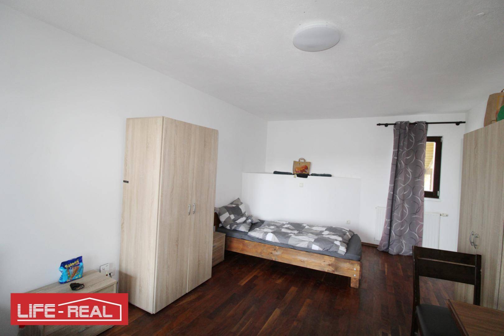 Gemütliches Schlafzimmer mit Holzbett, Kleiderschrank und Fenster mit Vorhängen.