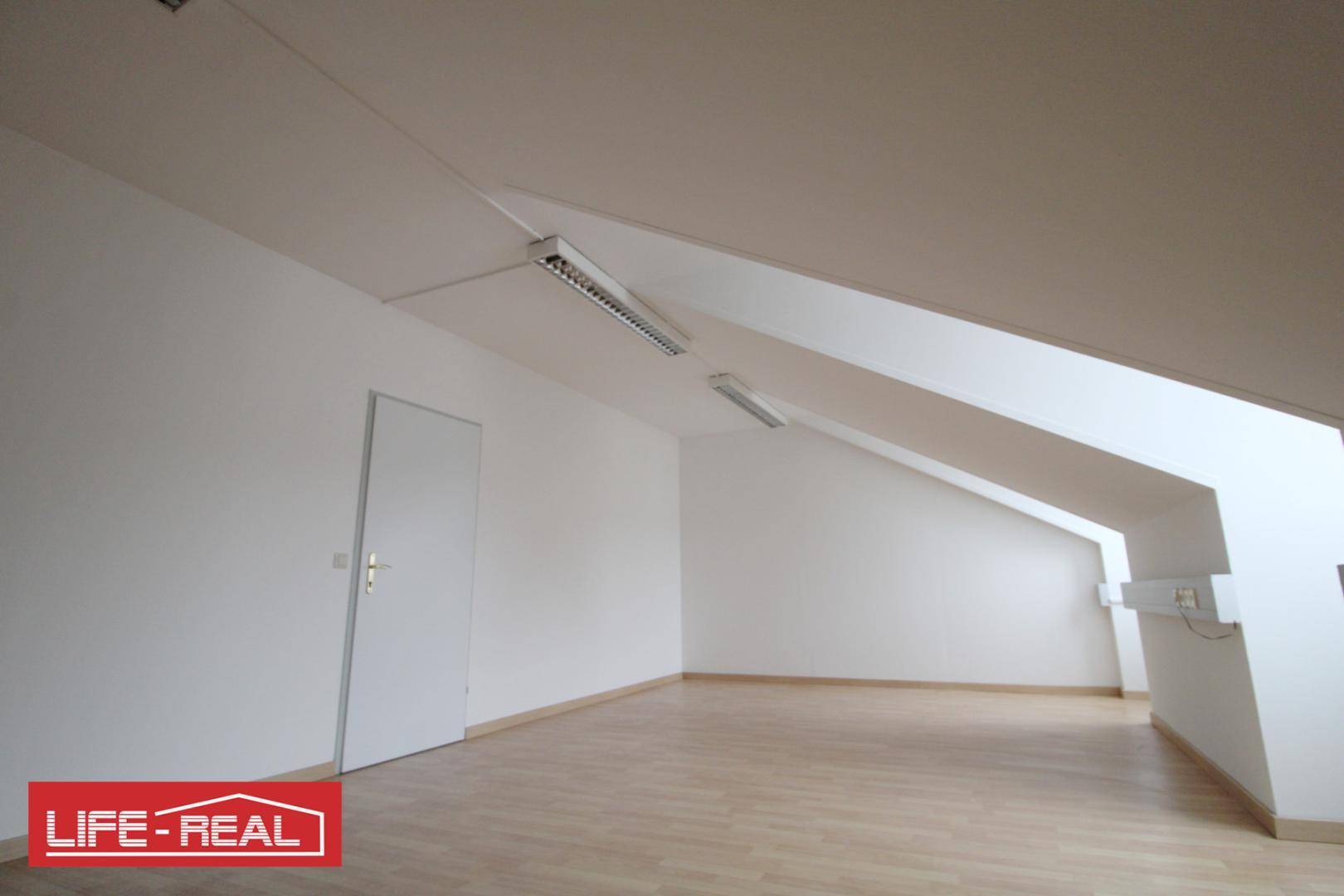 Heller Dachraum mit schrägen Wänden, Laminatboden und einer Tür, bietet Potenzial für individuelle Gestaltung.