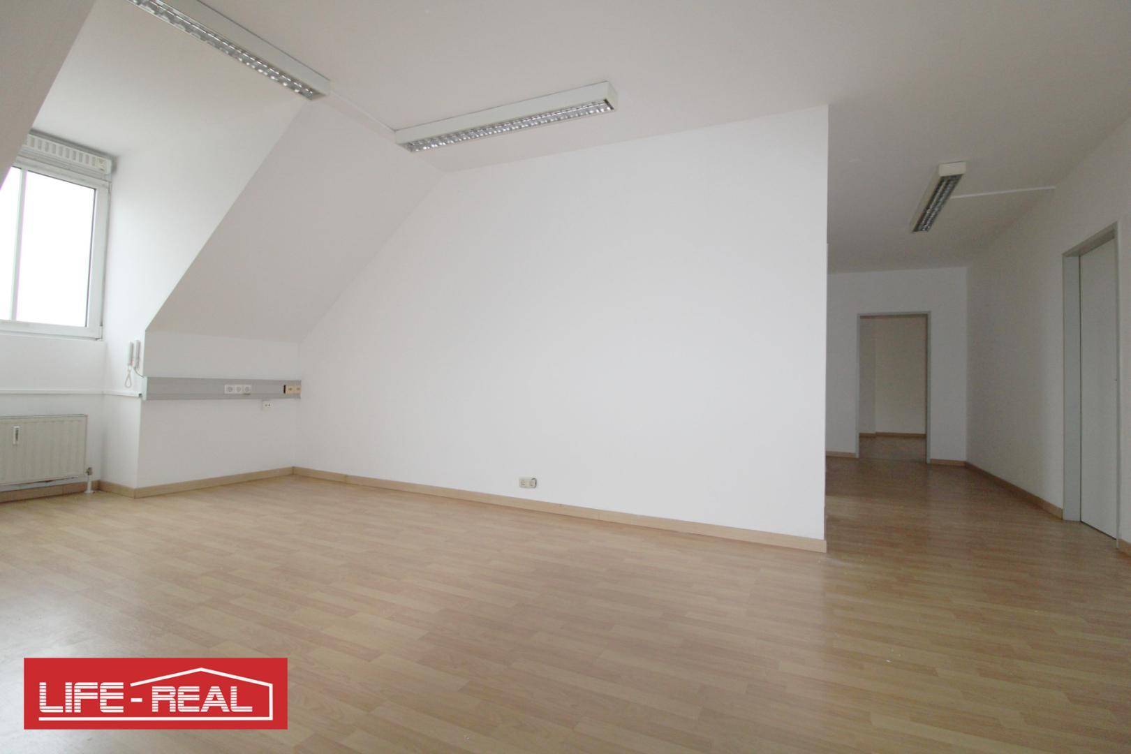 Offener Dachraum mit Laminatboden, einem Fenster und Zugang zu weiteren Bereichen, ideal für flexible Nutzung.