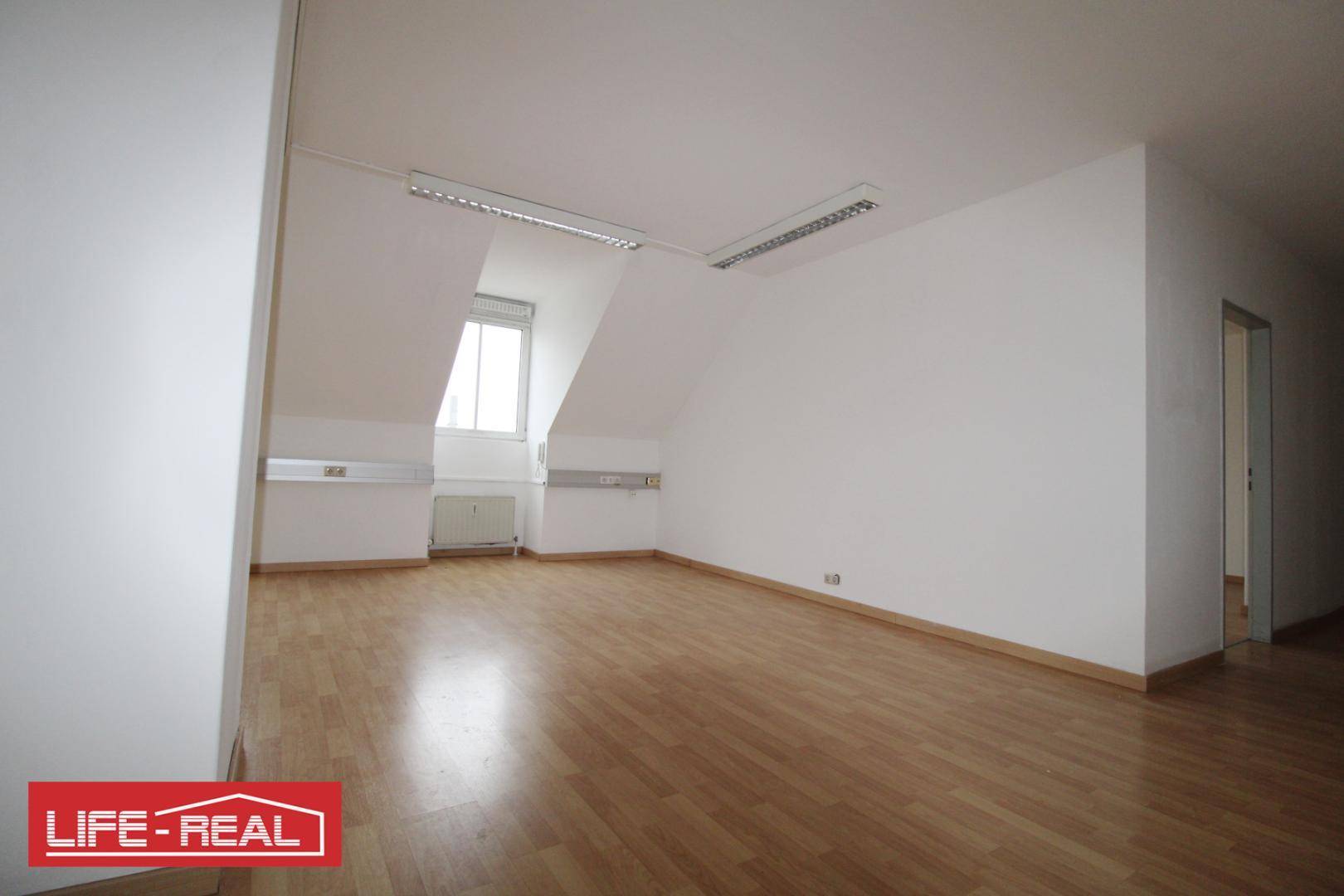 Heller Dachraum mit schrägen Wänden, Laminatboden und einem Fenster, das viel Tageslicht spendet.