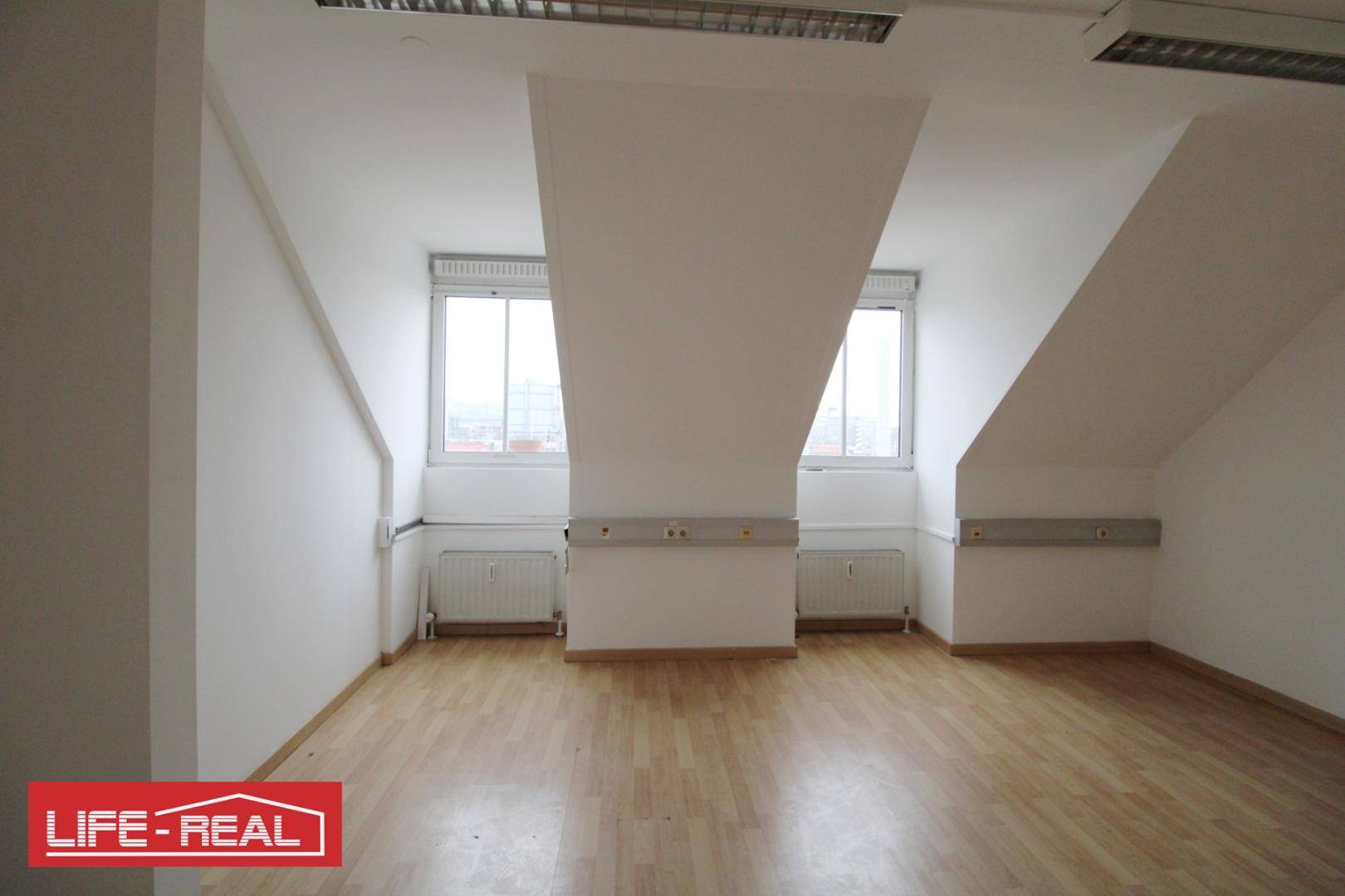 Heller Dachraum mit zwei Fenstern, Heizkörpern und Laminatboden, ideal für Büro oder Wohnzwecke.