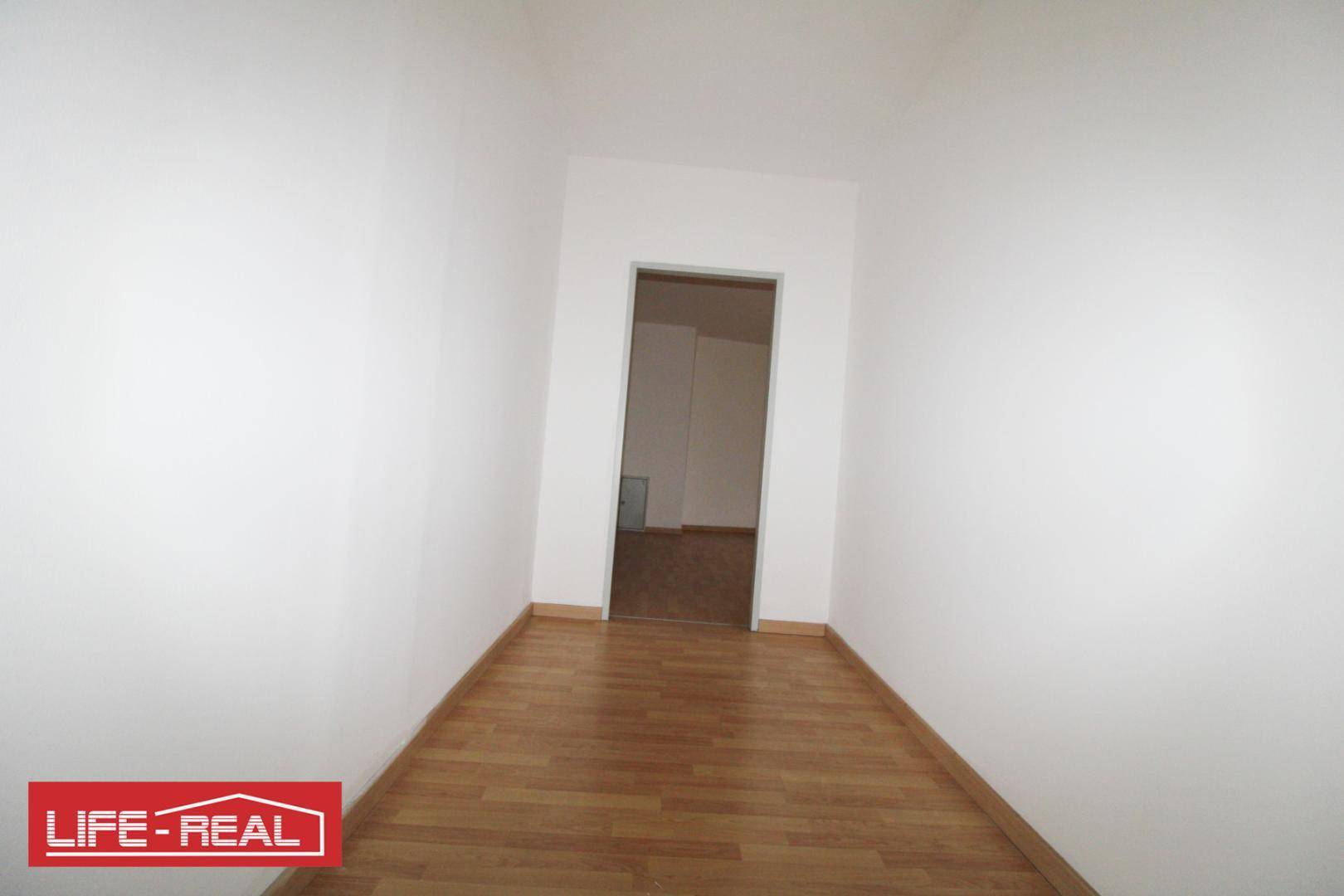 Schmaler Flur mit Laminatboden und weißen Wänden, der zu einem weiteren Raum führt.