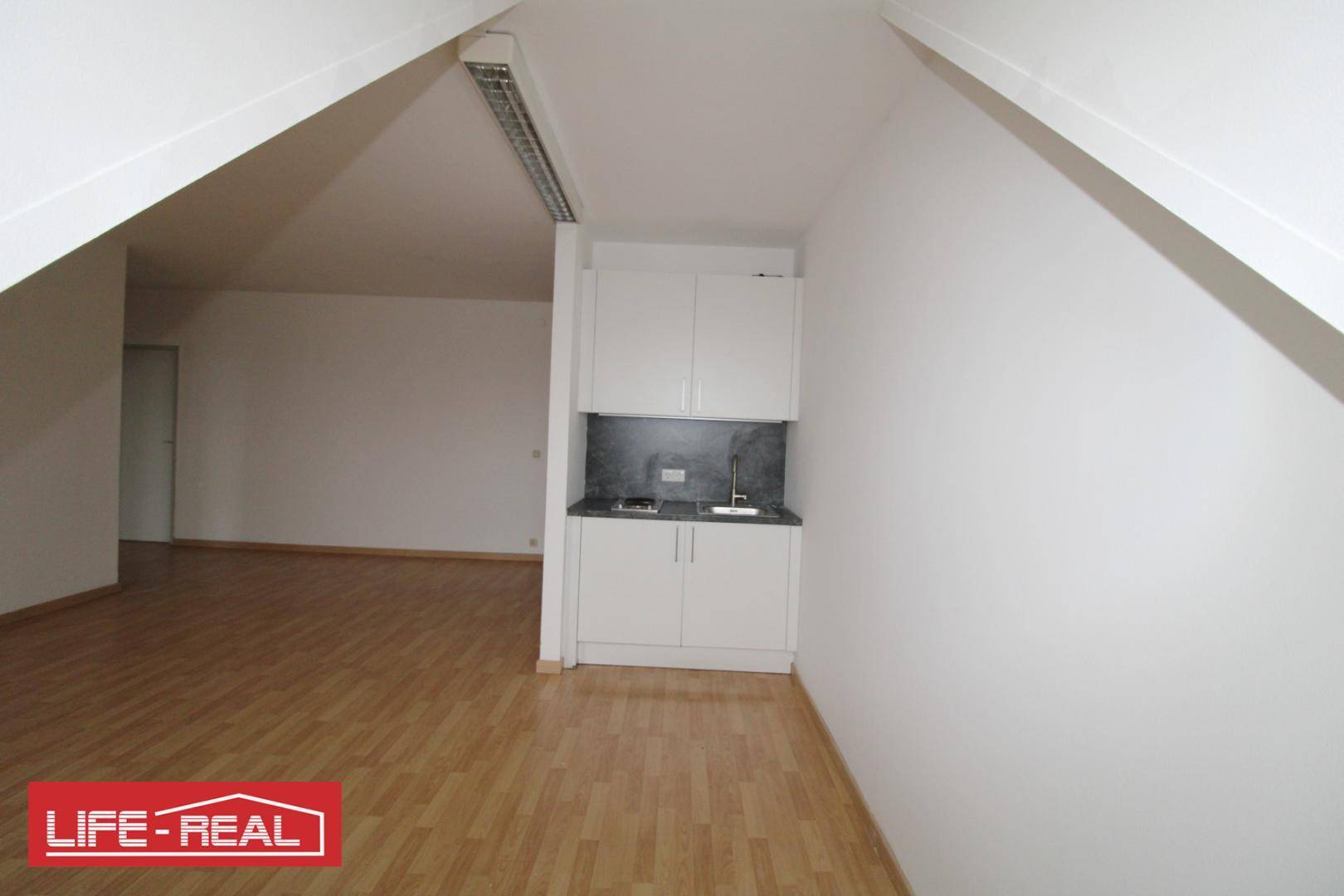 Kompakte Küchenzeile in einem Dachraum mit Laminatboden und weißen Schränken, praktisch und funktional.