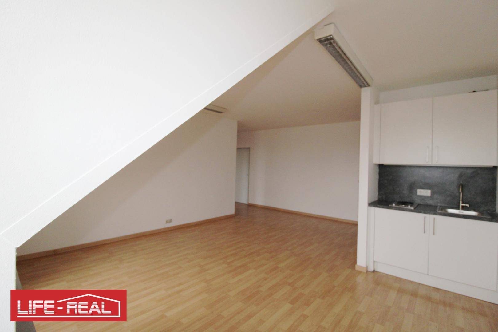 Dachraum mit integrierter Küchenzeile, Laminatboden und schrägen Wänden, ideal für ein kleines Büro.