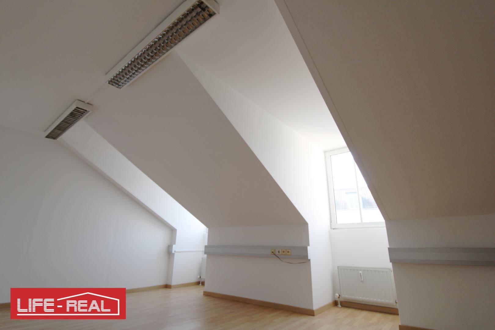 Dachraum mit schrägen Wänden, Laminatboden und einem Fenster, das natürliches Licht hereinlässt.