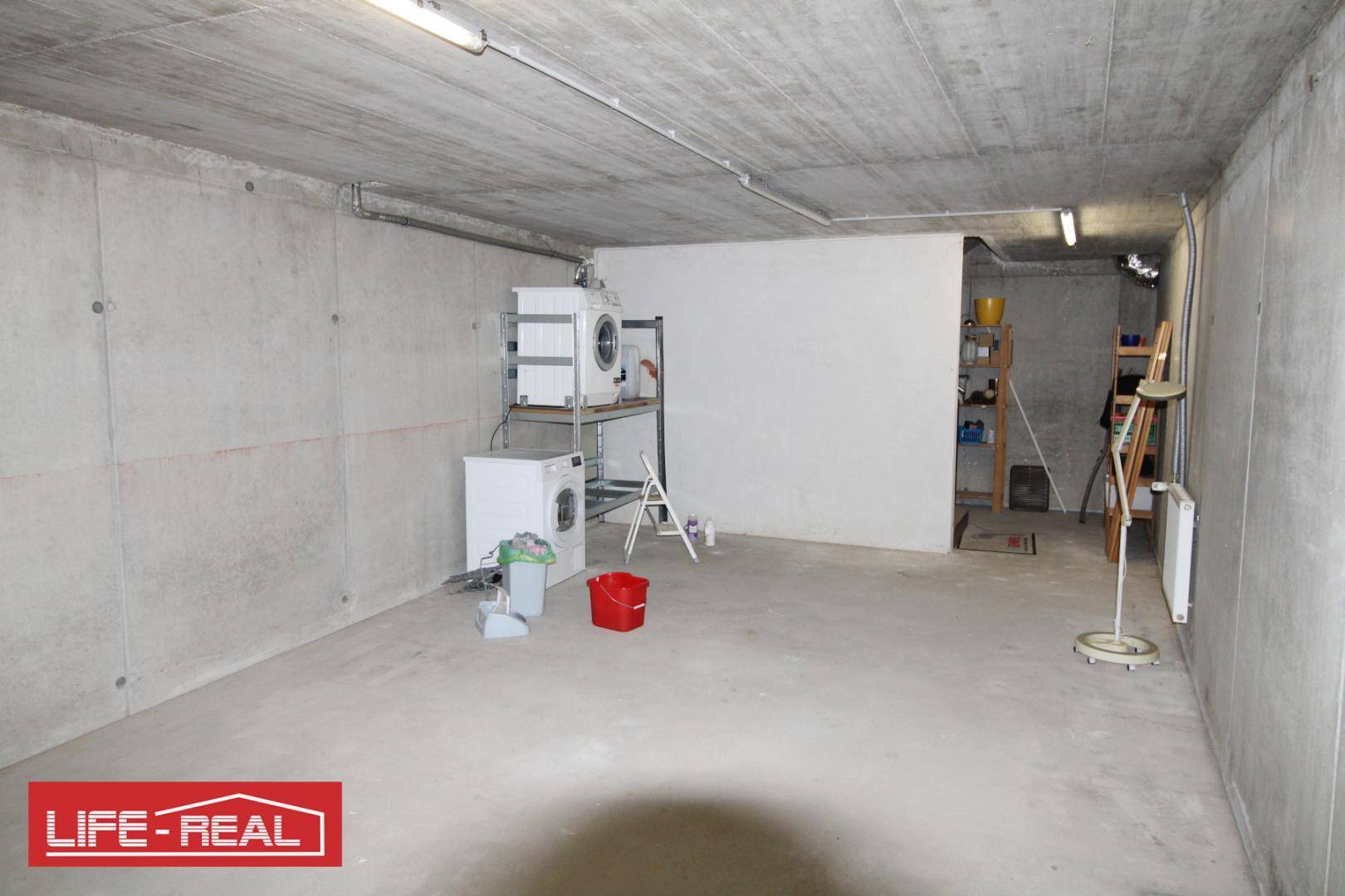 Geräumiger Kellerraum mit Betonwänden und -boden, ausgestattet mit Waschmaschinen und Regalen.