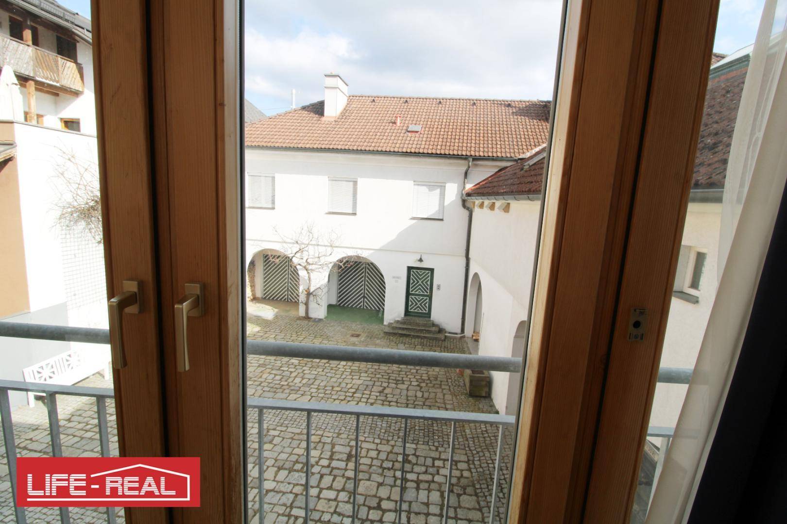 Blick vom Balkon auf einen gepflasterten Innenhof mit historischen Gebäuden und Arkaden.